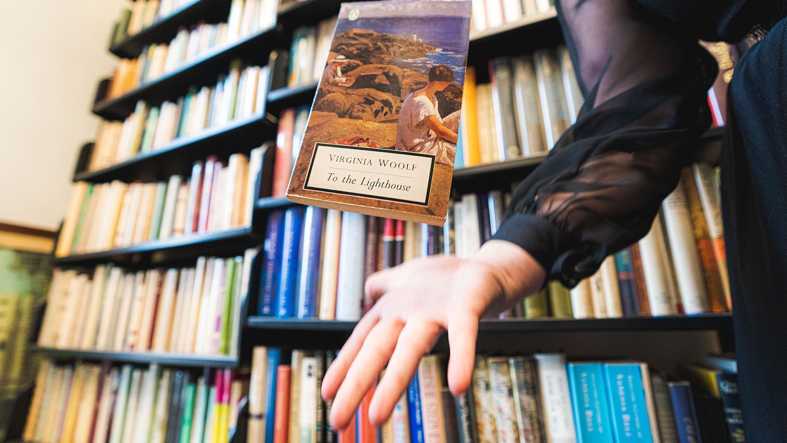 Virginia Woolf's To The Lighthouse floats above a hand, in the background are rows of books
