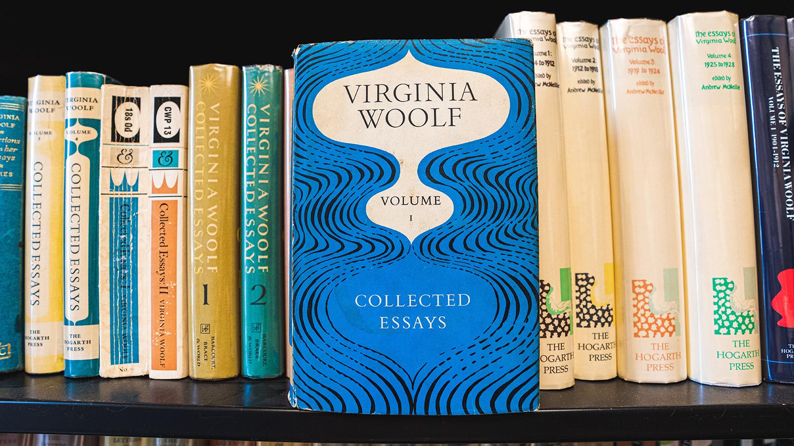 A blue copy of Virgina Woolf's collected essays stands upright in front of a row of books