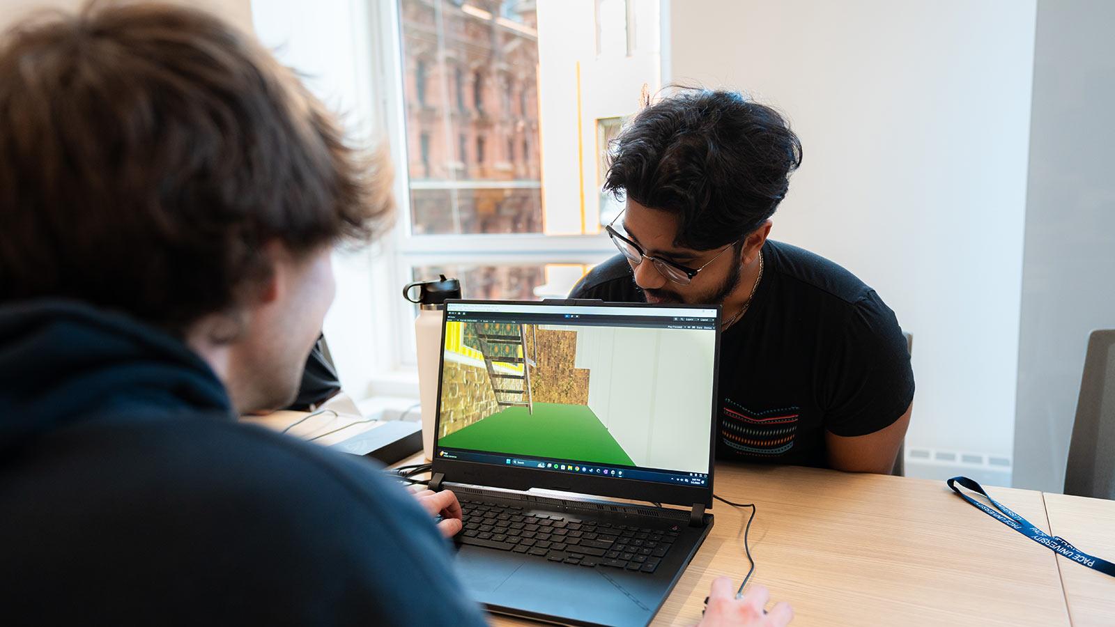 Two Pace University students sit on opposite sides of a laptop playing a game