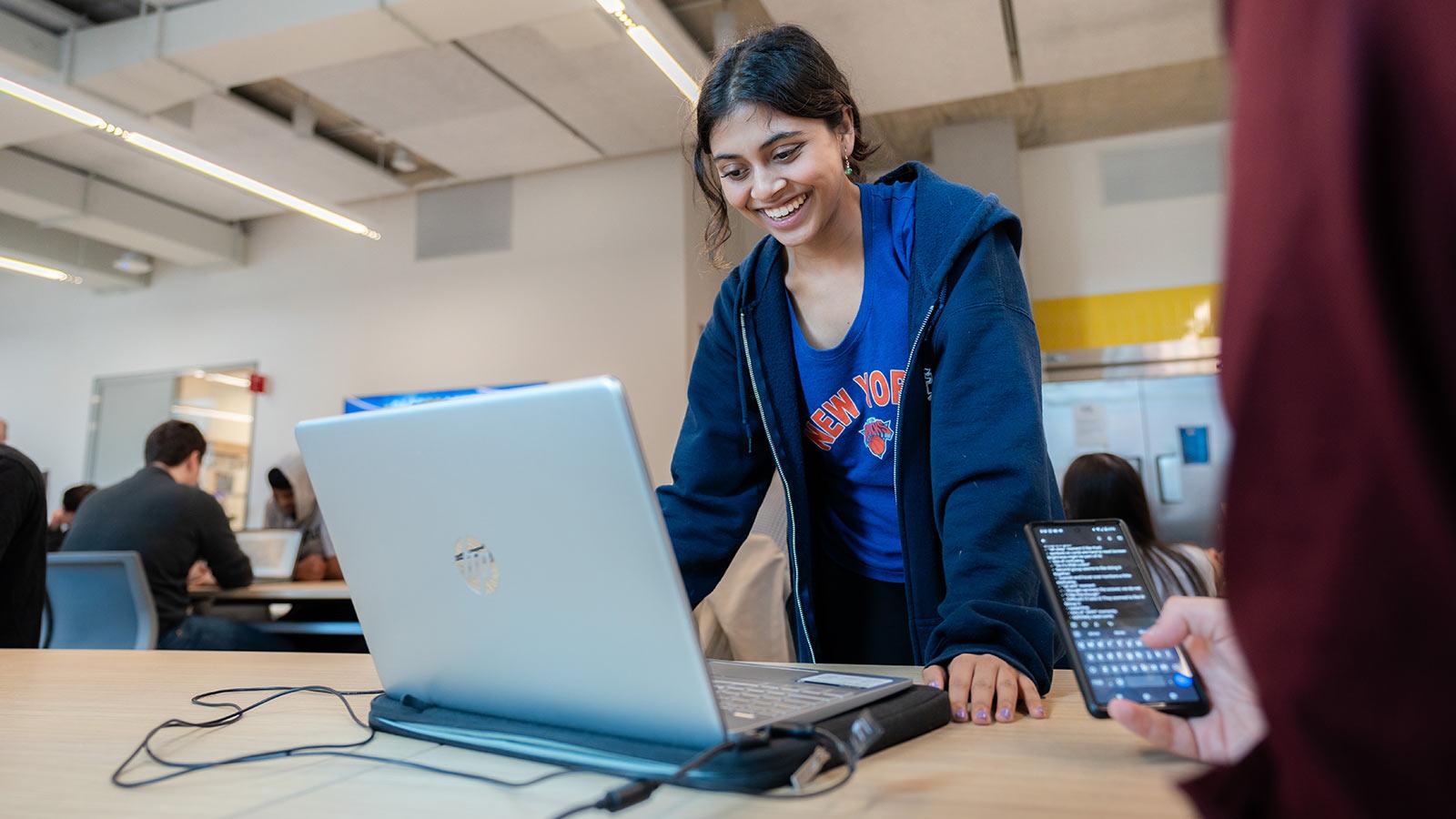 A Pace student in a blue sweater stands at a laptop
