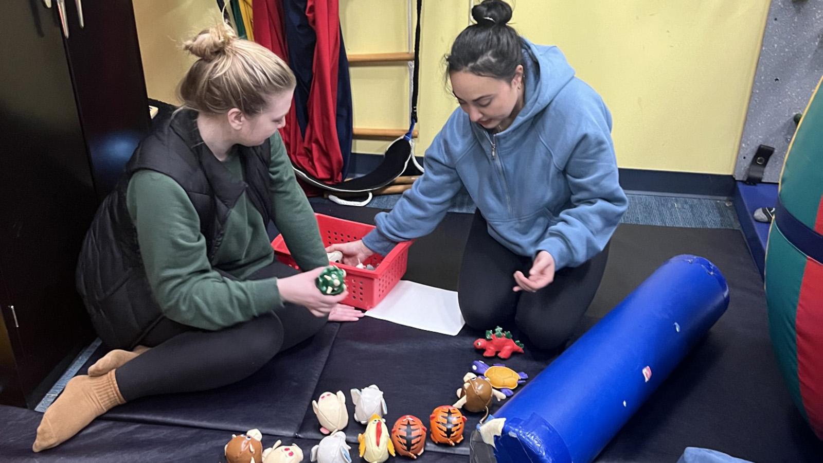 Two Pace University College of Health Professions students sitting on ground playing with sensory toys.
