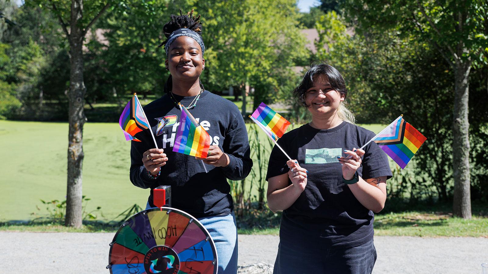 Two Pace University students smiling at the camera and holding pride flags at the campus involvement fair on the Westchester campus.