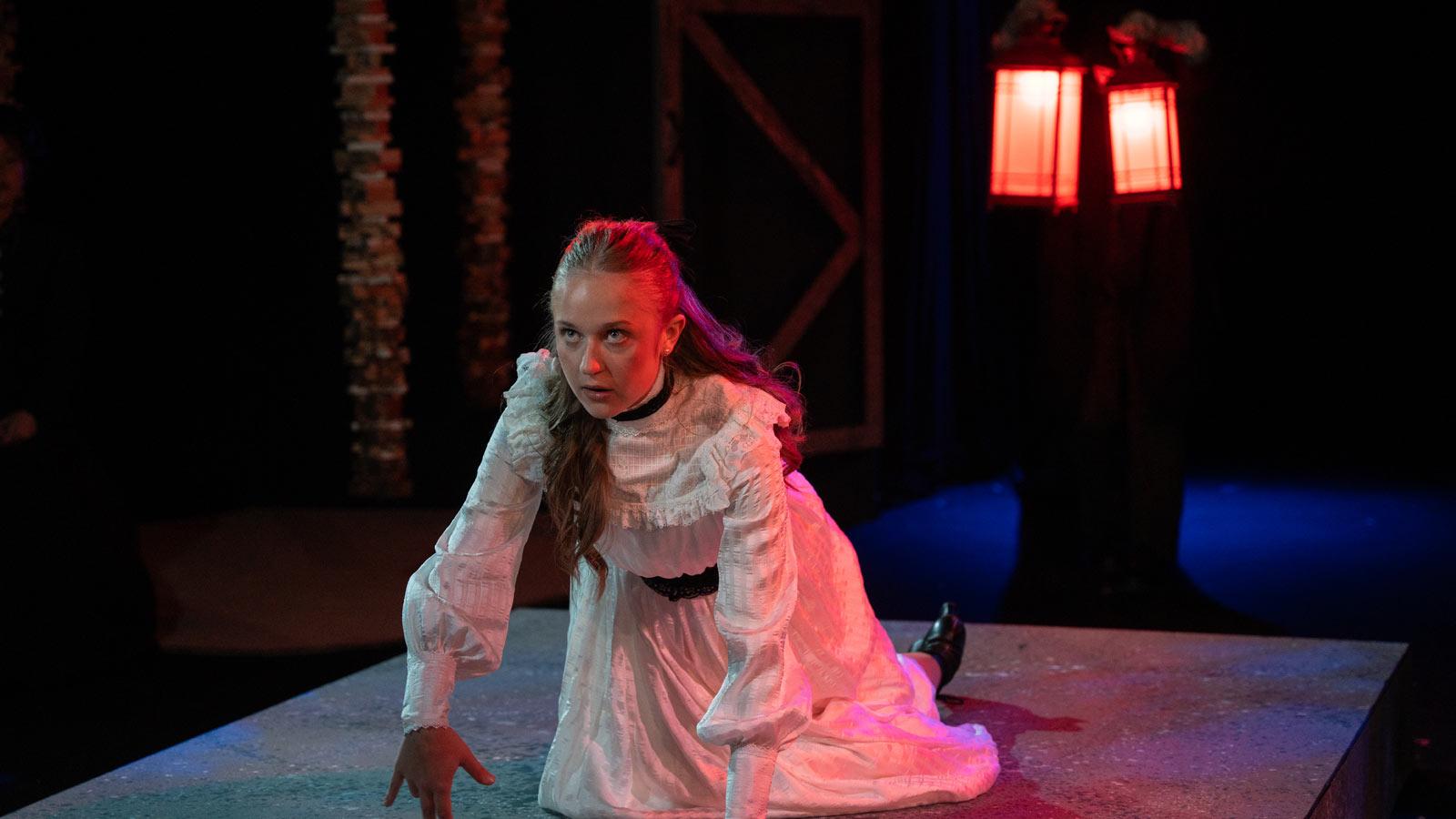 Actor kneeling on stage in costume.