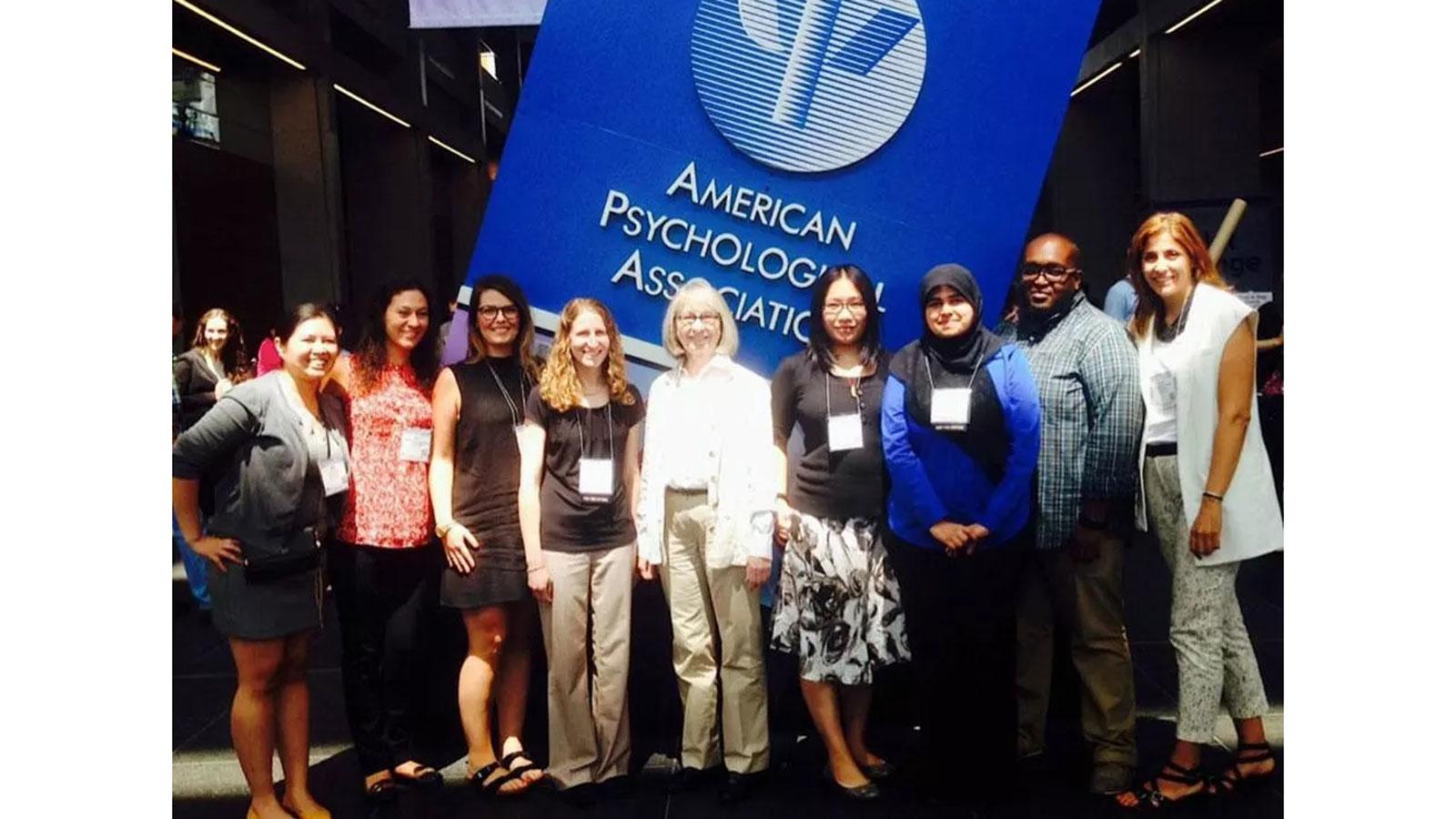 Pace University Psychology Parent Child Institute team members standing together at the American Psychology Association (APA) conference with APA logo in background
