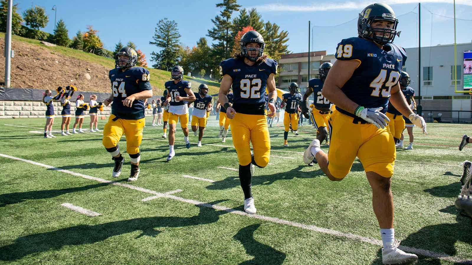Pace University football players running on the field at Homecoming.