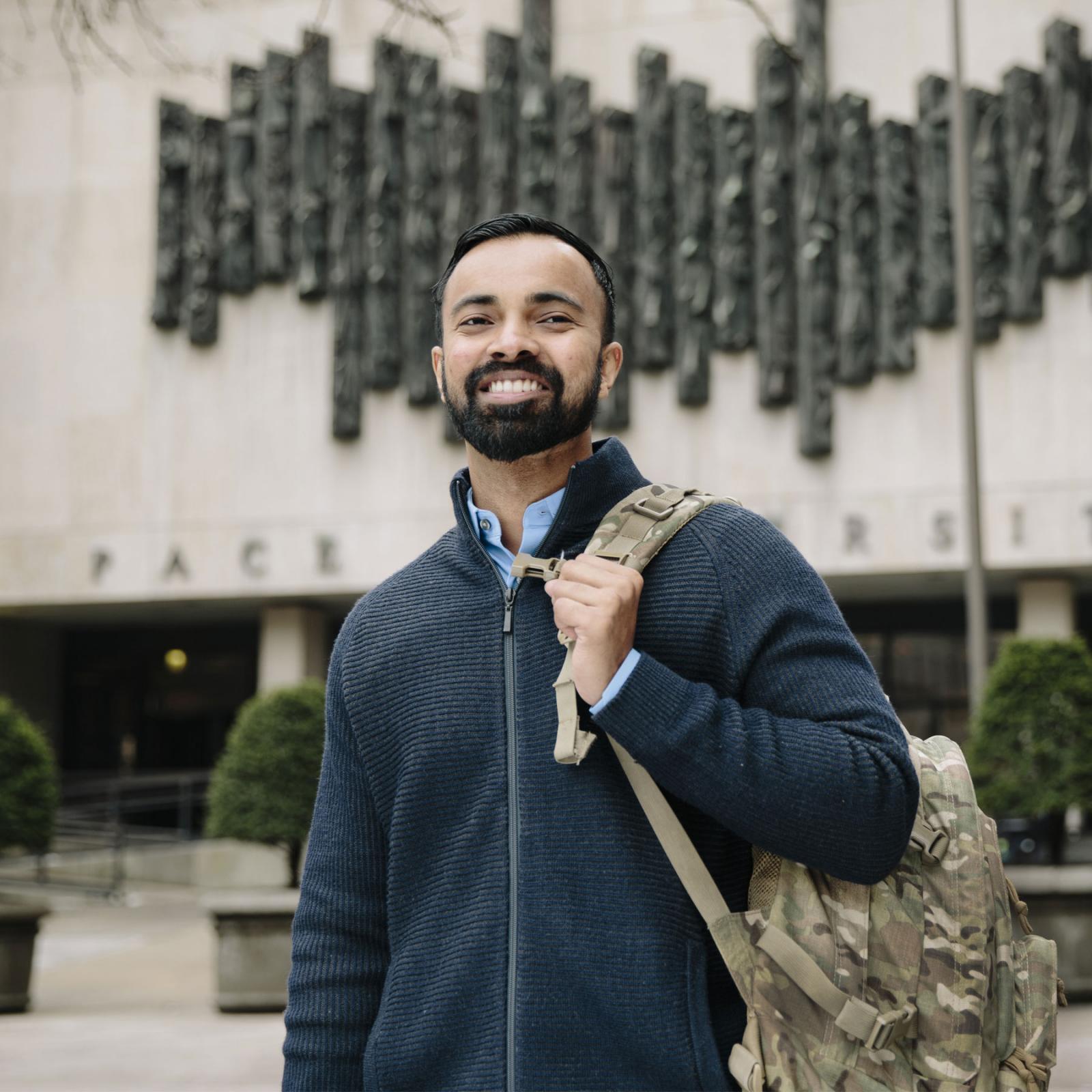 Veteran student smiling at the camera holding a backpack.