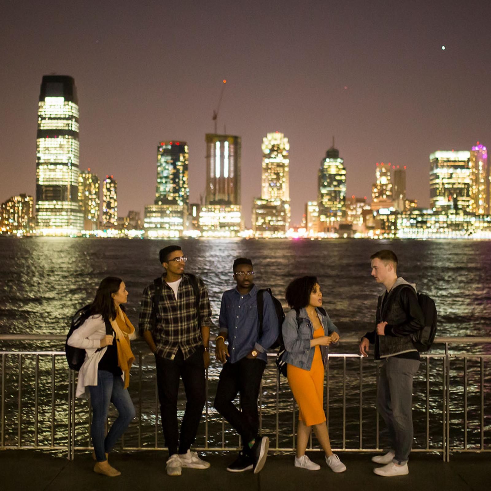 Students at Battery Park at night looking over the Hudson river