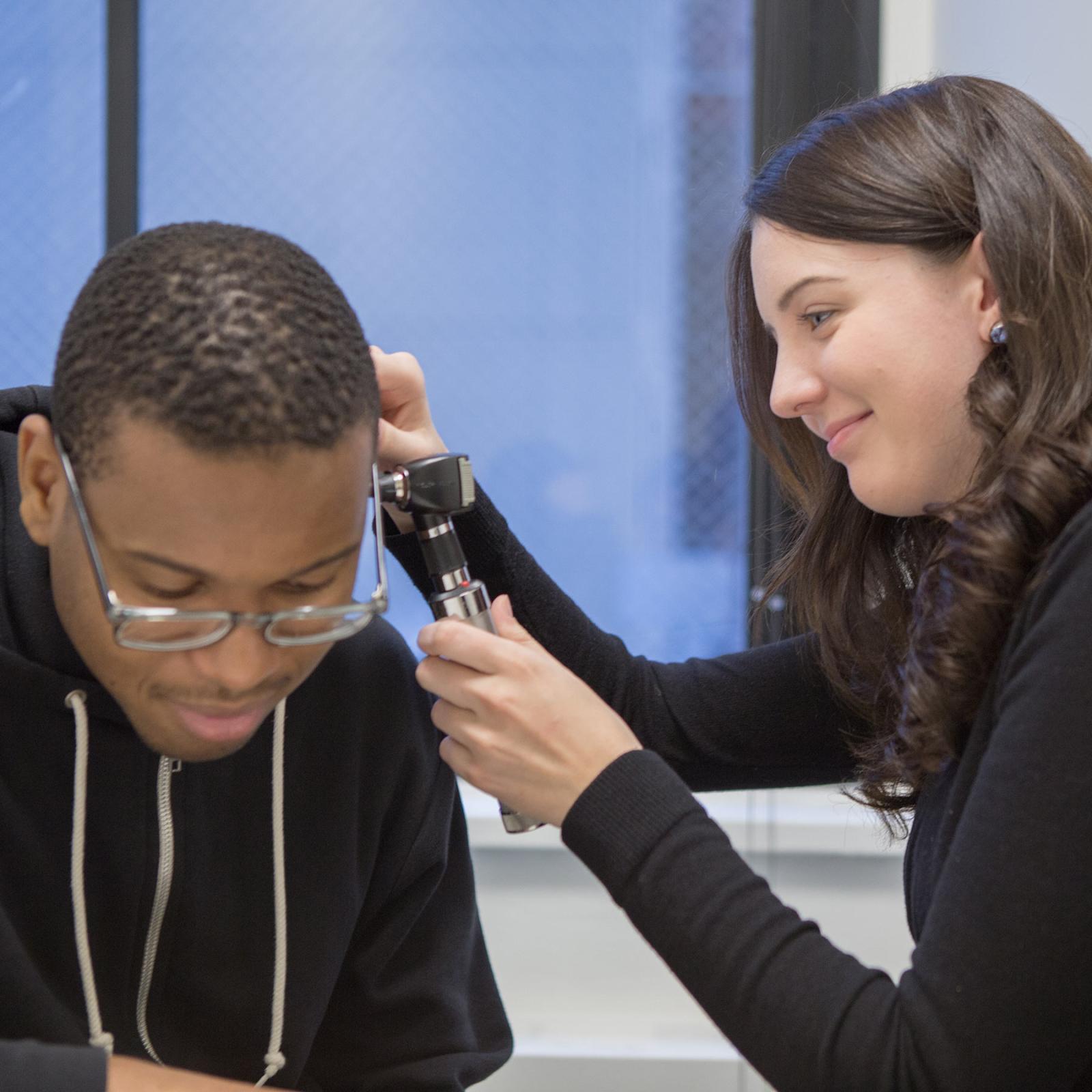 Student looking into a patient's ear.