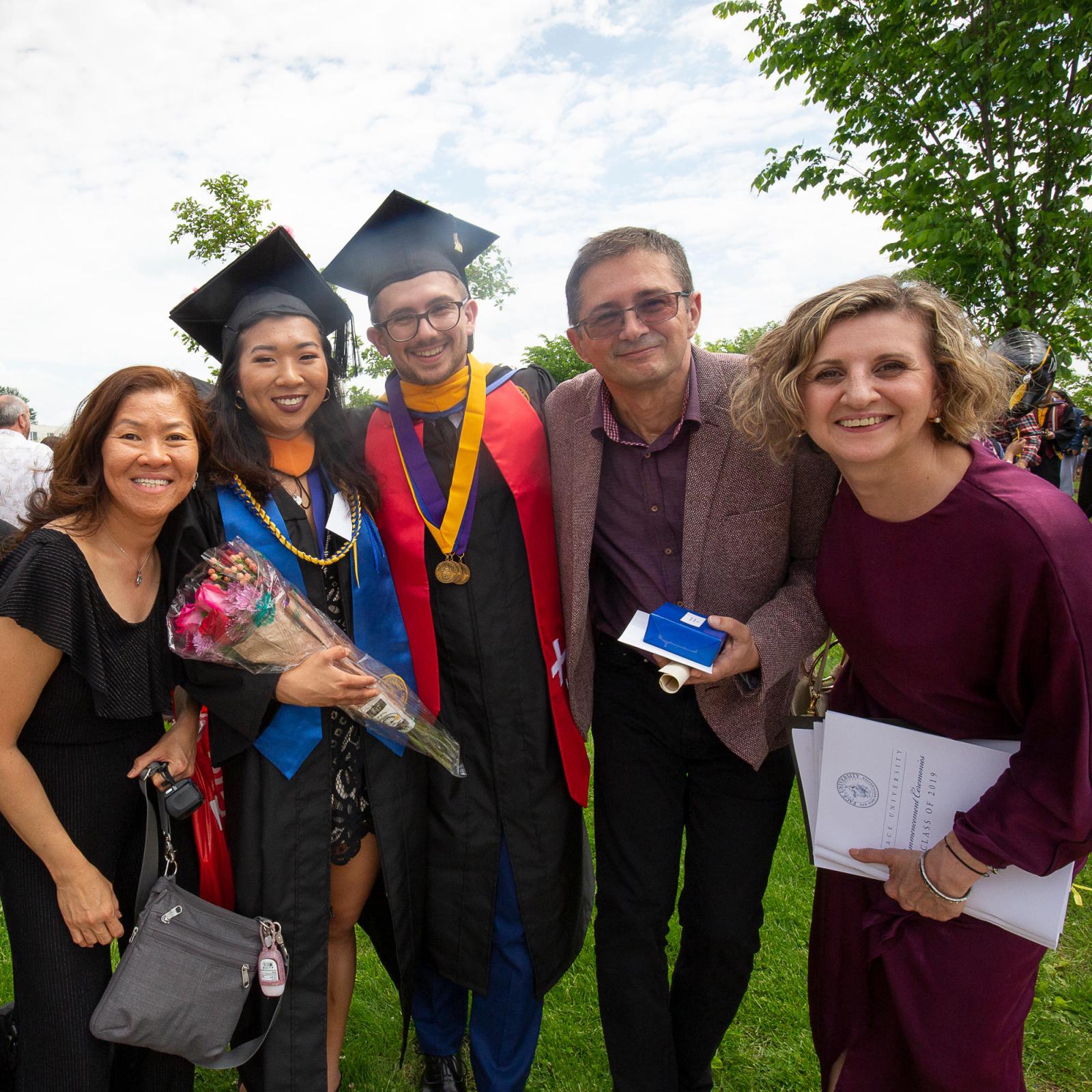 Pace student at his Commencement ceremony with his family, smiling at the camera.