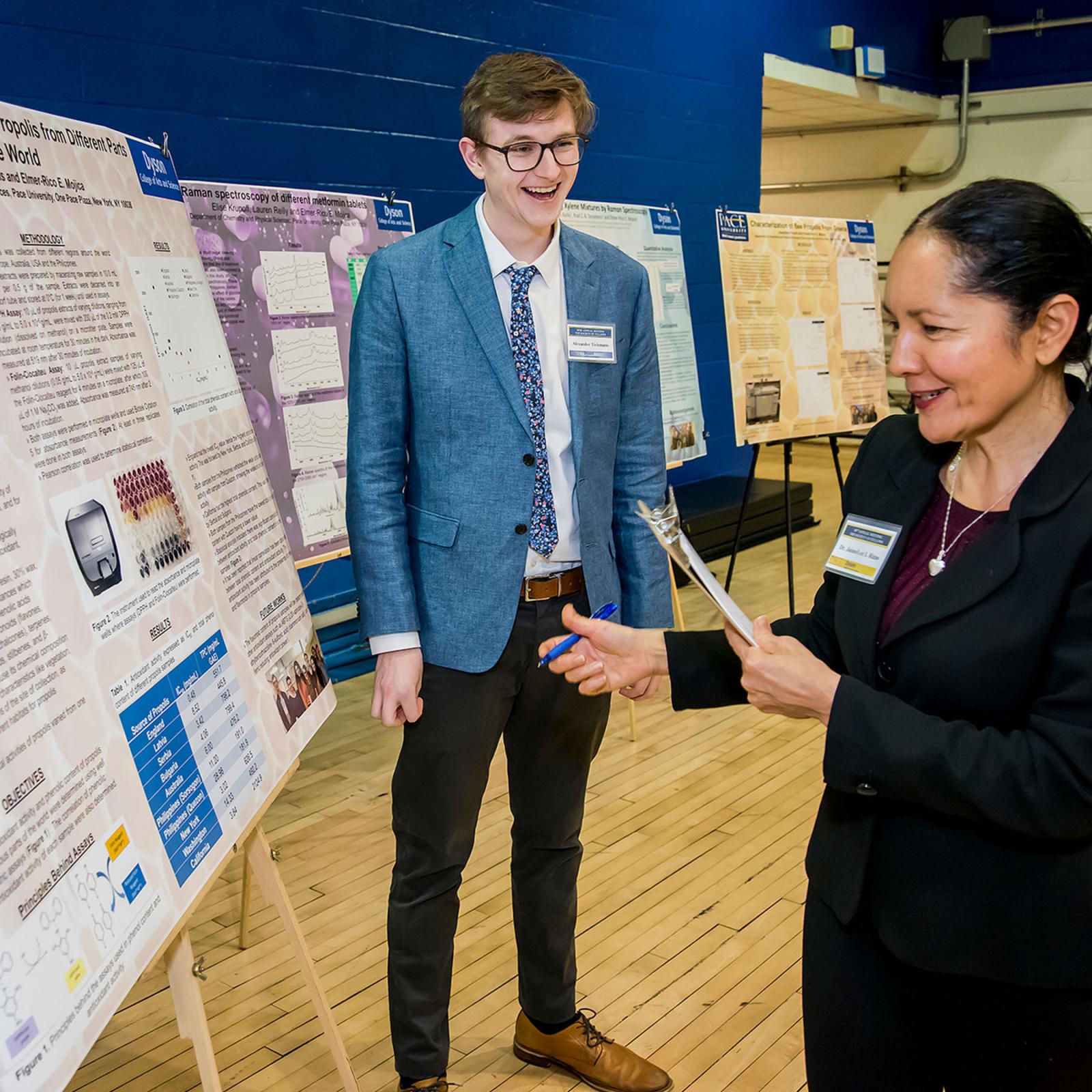 Male student standing infront of his research poster as a facutly member reads