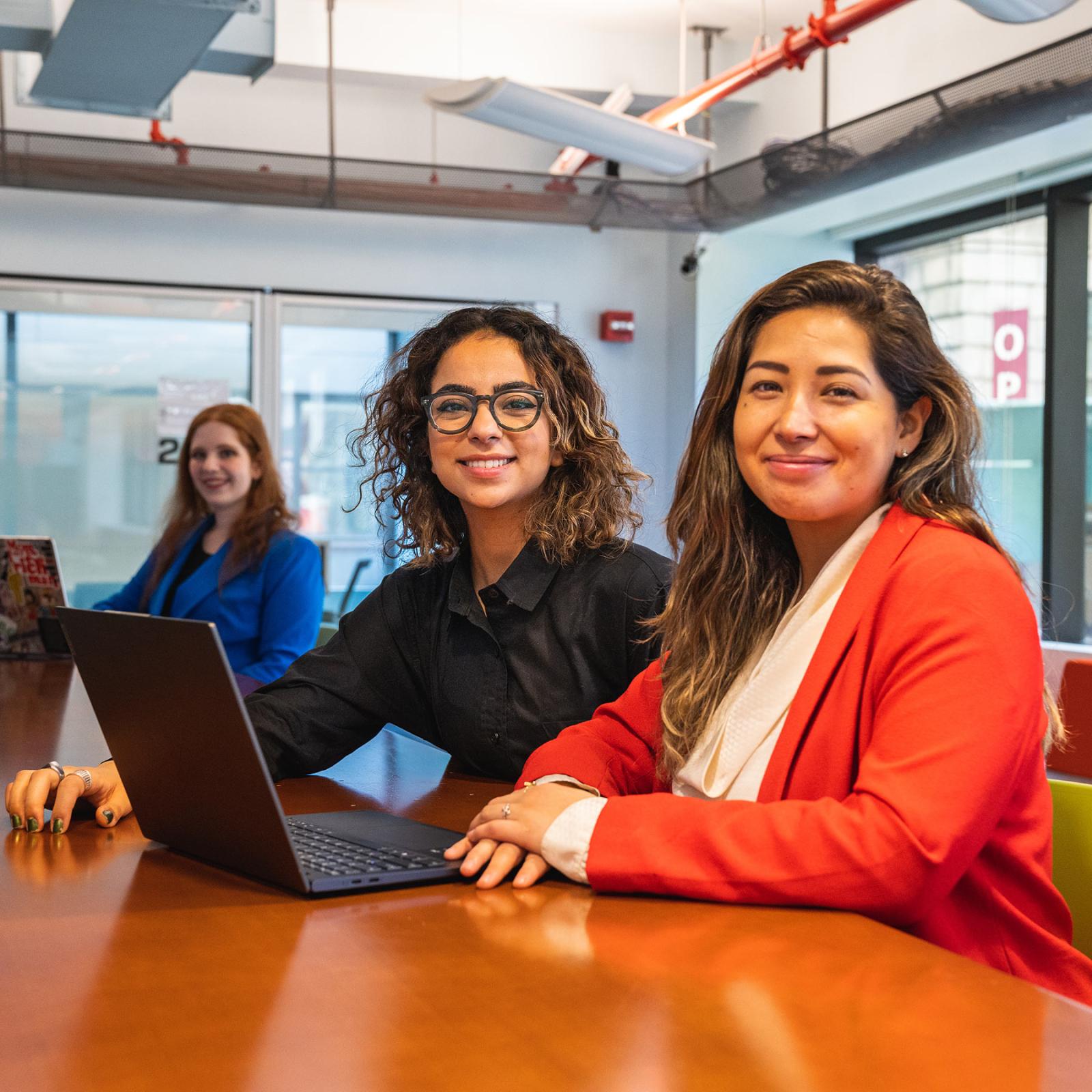 Two women sitting in front of a laptop smiling at the camera.