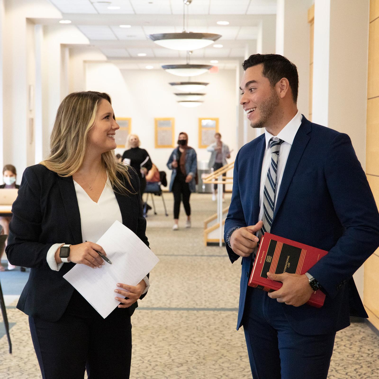 Two law students standing in the hallway, holding books and laughing.