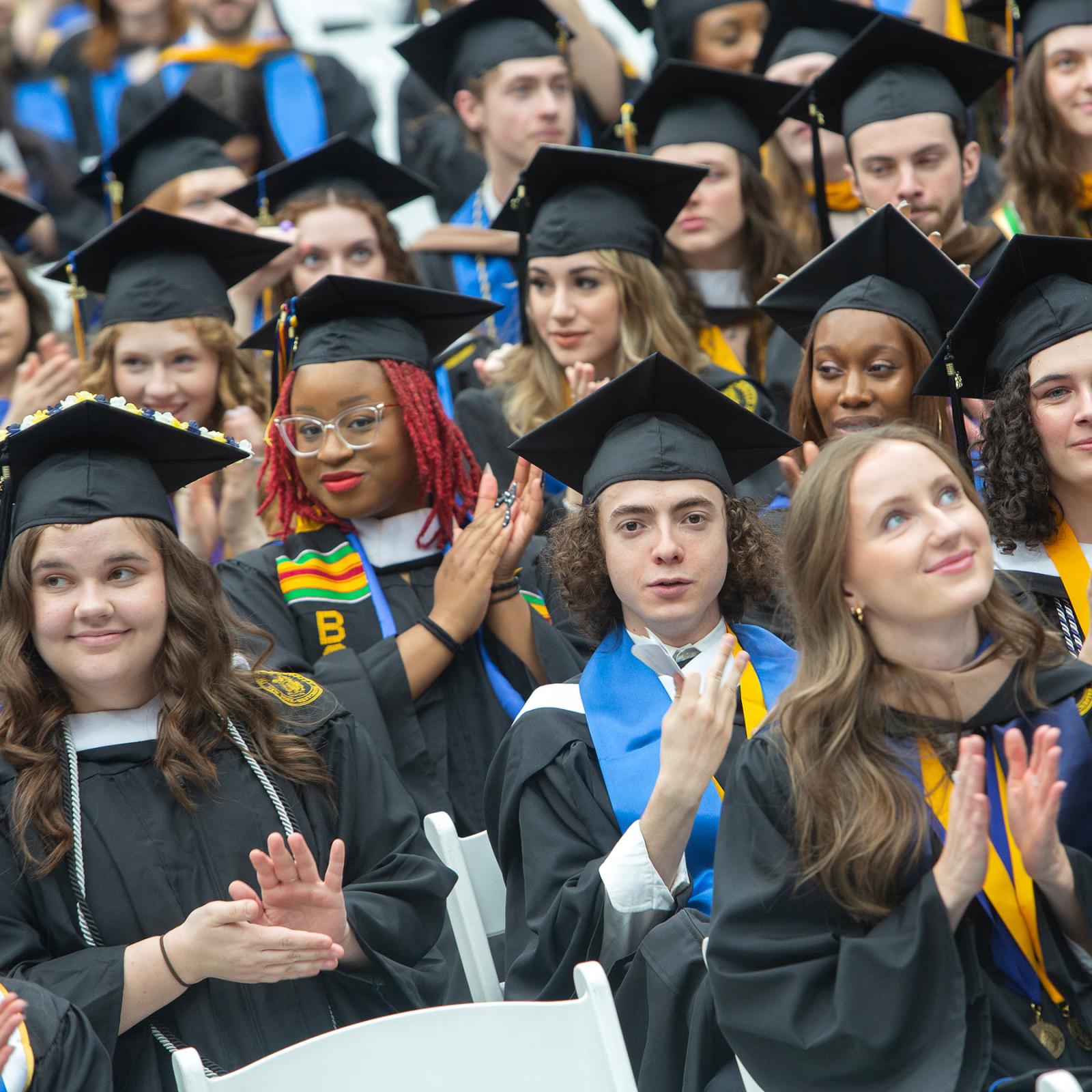 Group of Pace student at their Commencement ceremony, clapping and smiling at the camera.