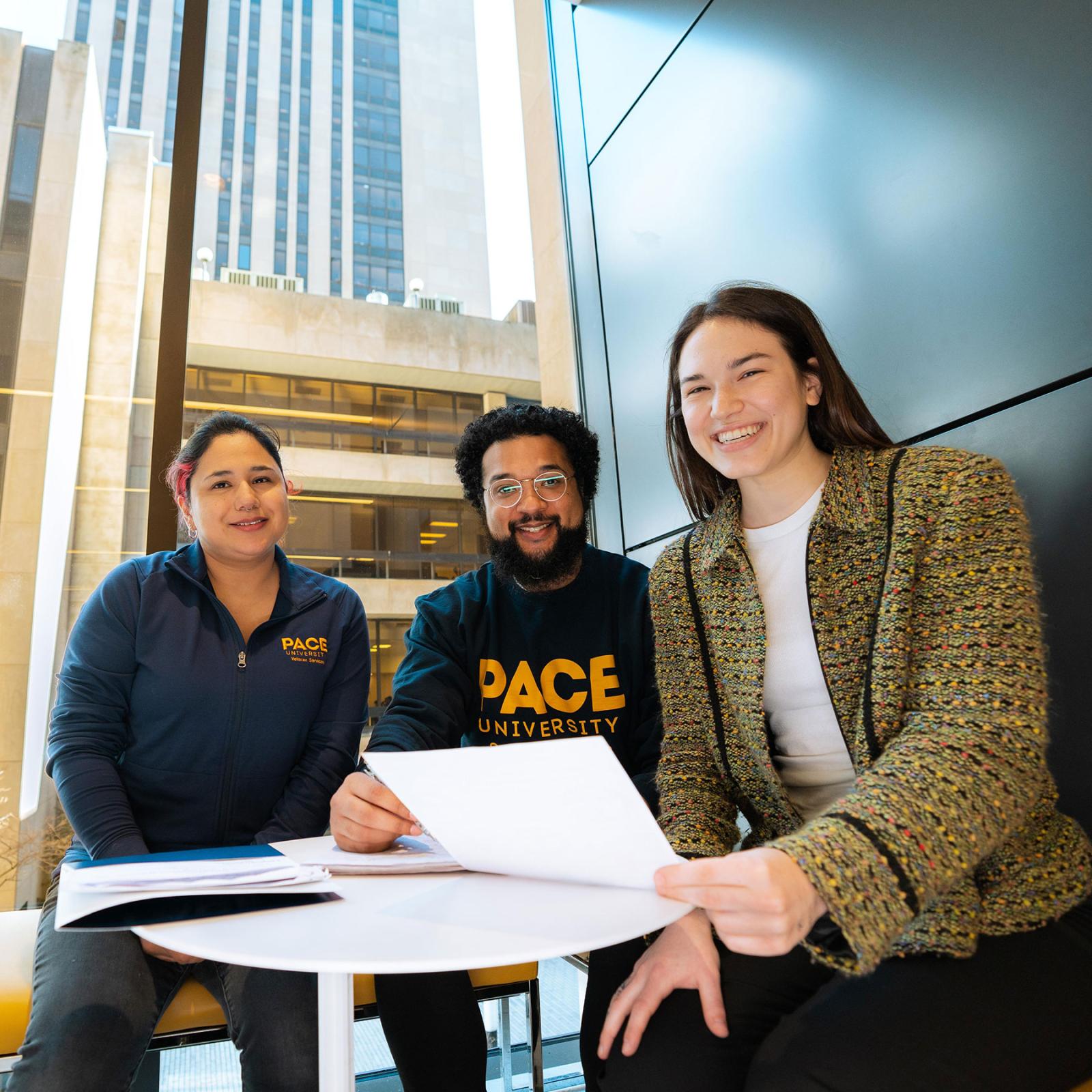 three pace students holding a piece of paper and posing for the camera