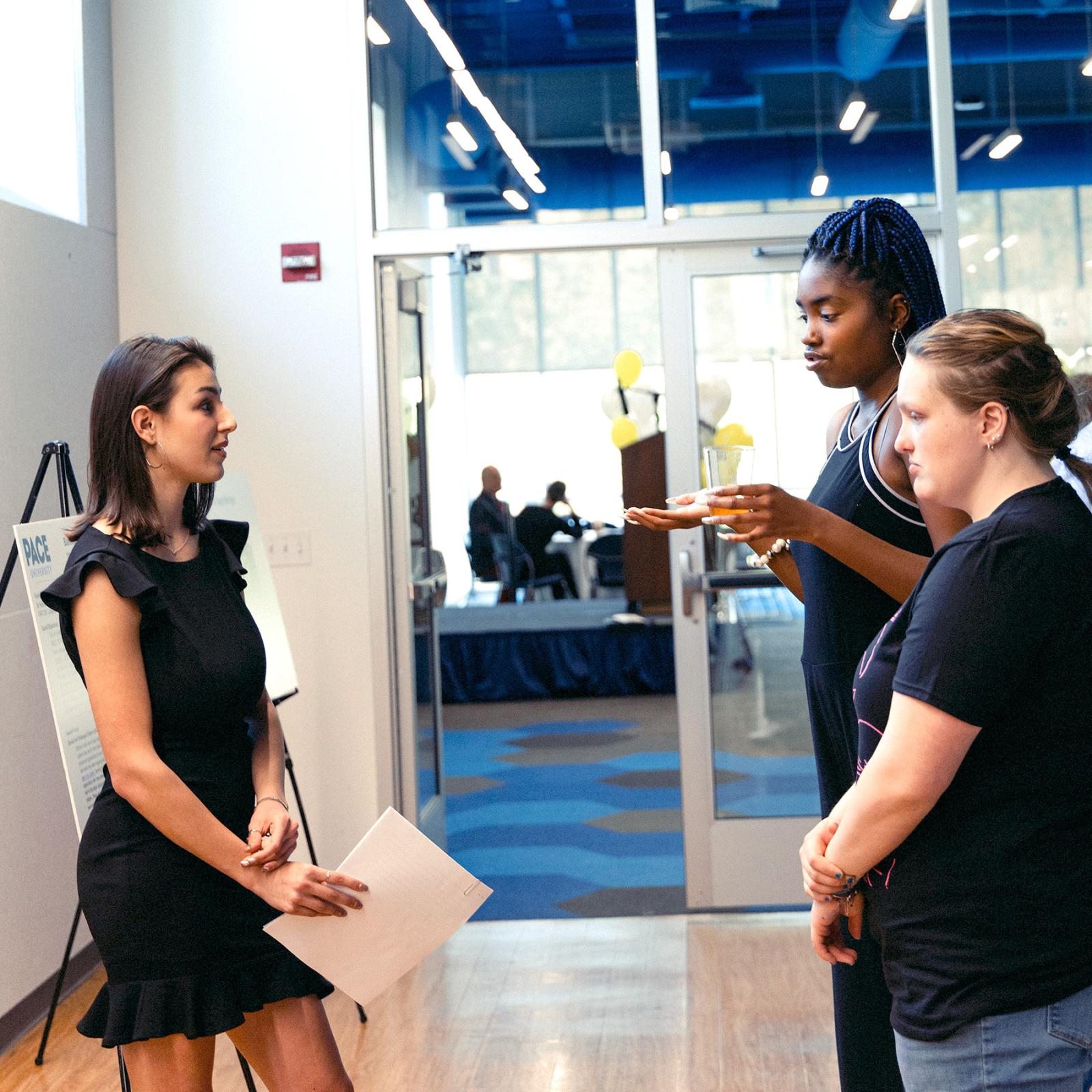 Pace University's Writing and Cultural Studies student Nicolina Baron explaining her research to two female students