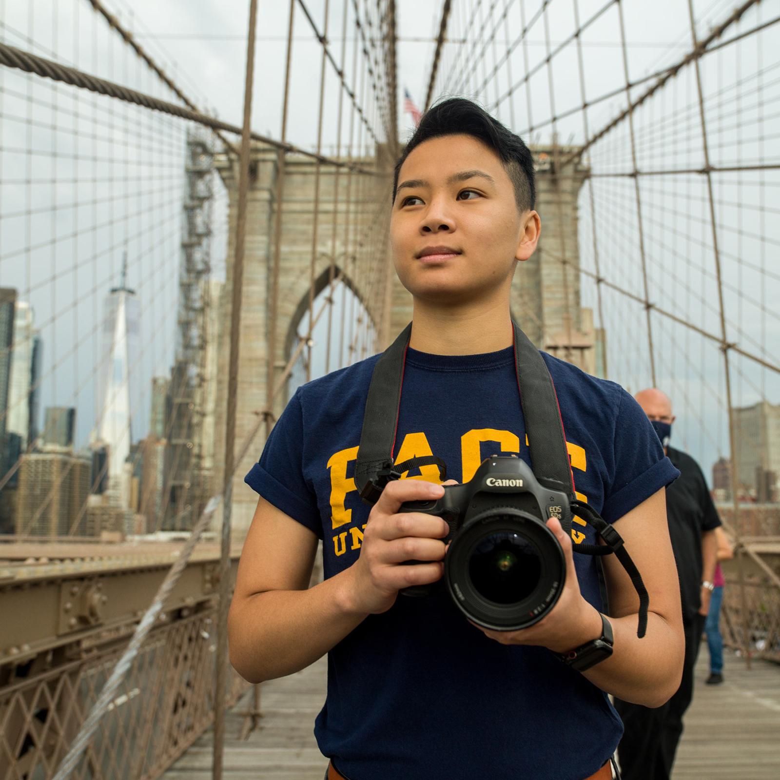 A Pace student poses on the Brooklyn Bridge with his camera