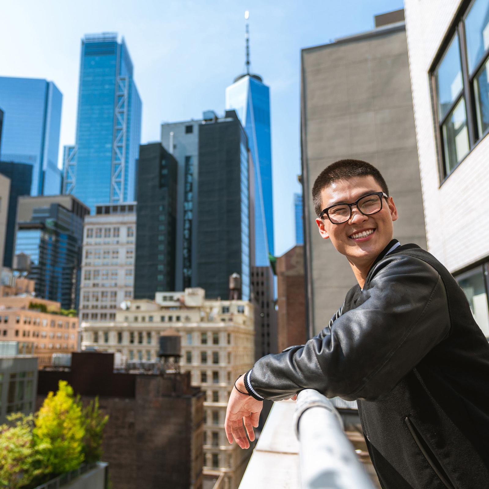 a Pace student leans on a balcony with Manhattan buildings in the background