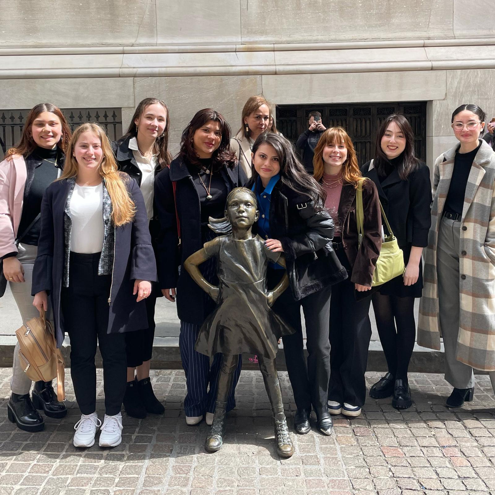 Group of Pace University Dyson College of Arts and Sciences students in the Womens Leadership Initiative standing together by the fearless girl statue