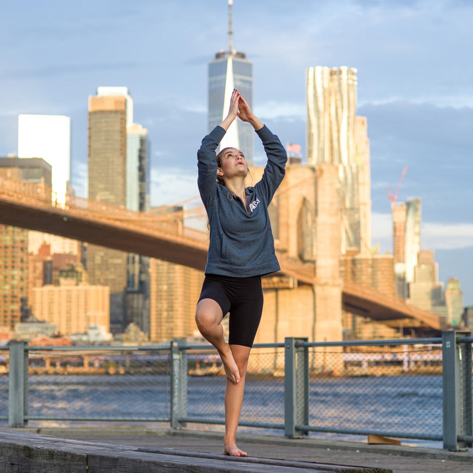 Pace university student doing yoga with the Brooklyn Bridge and New York City in the background