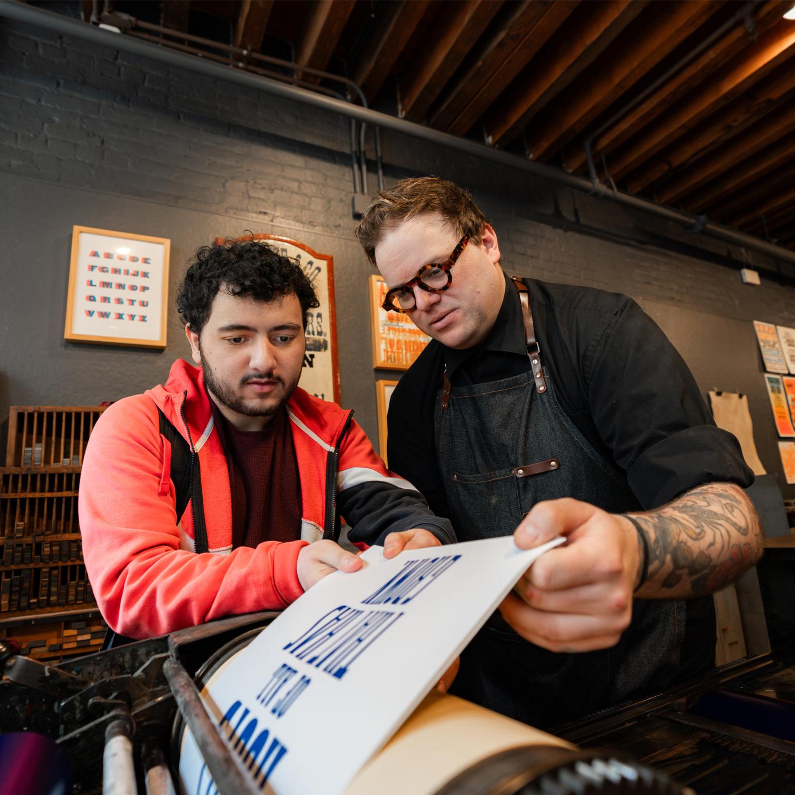 A Pace University student and professor working on a printing press.