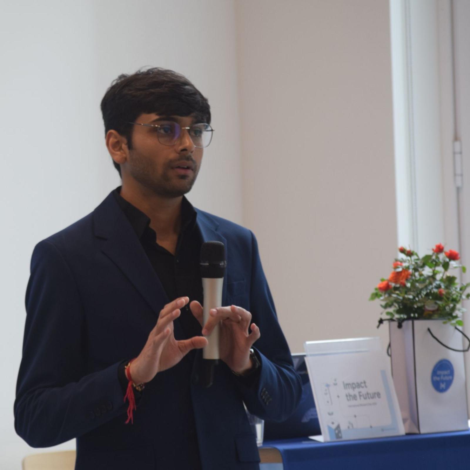 Pace student Om Gaikhe holding a microphone while giving a speech during an event presentation.