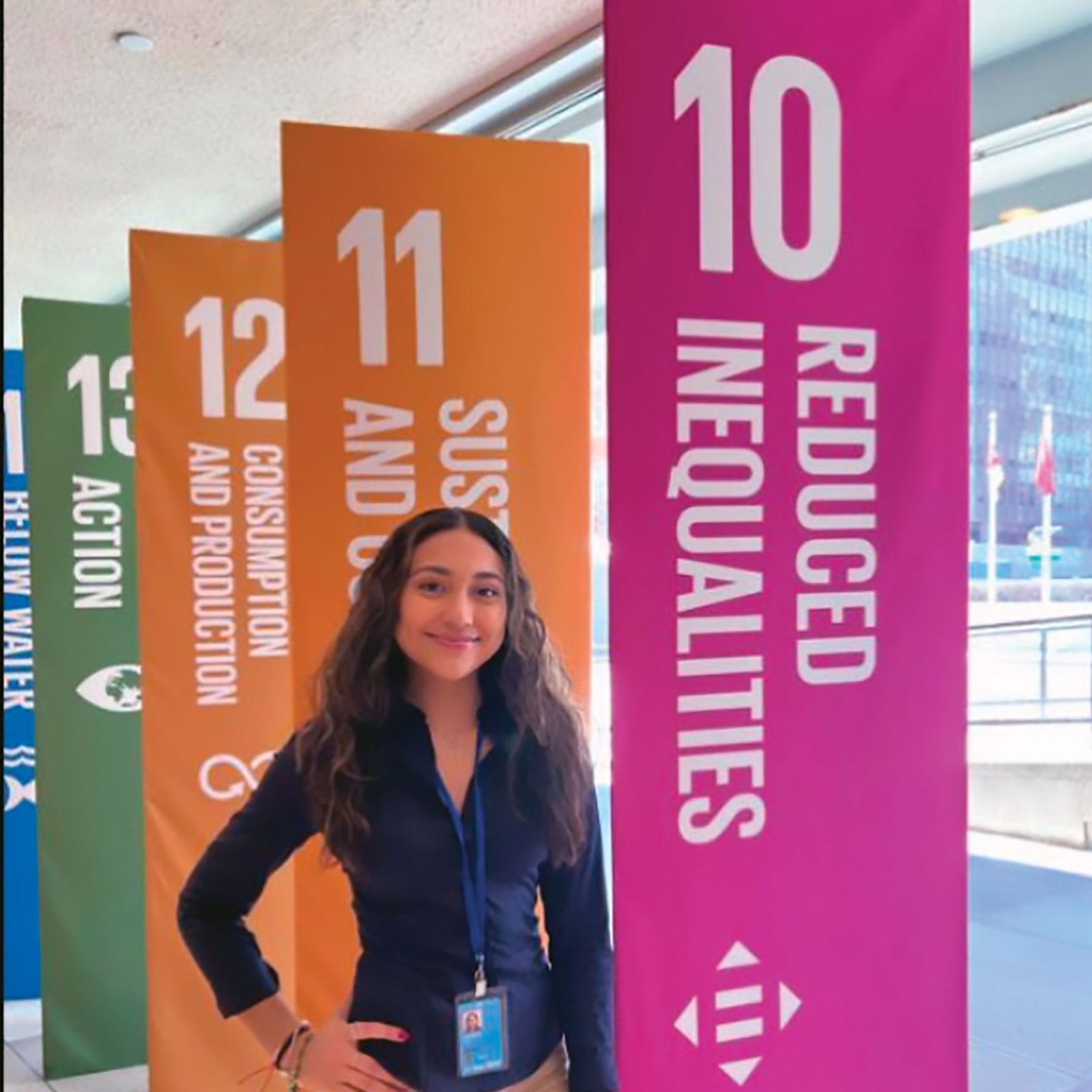 Pace University Women's and Gender Studies student standing by multicolored flags hanging from the ceiling
