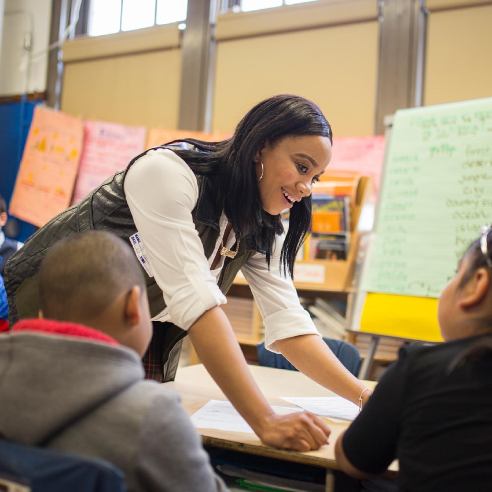 A teacher leaning over a table with young students.