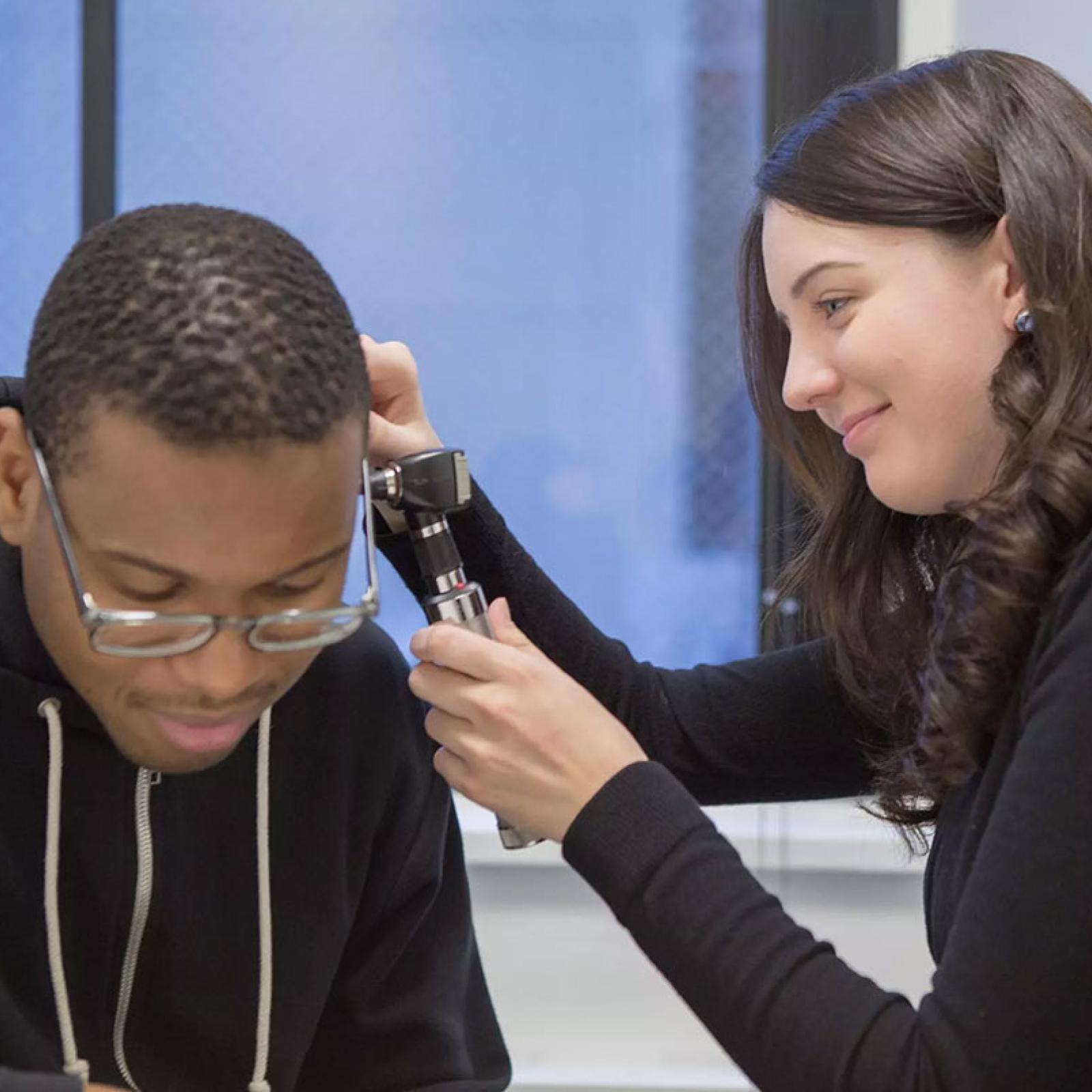 Pace University student in the Communication and Sciences Disorders, MS program looking into another student's ear.