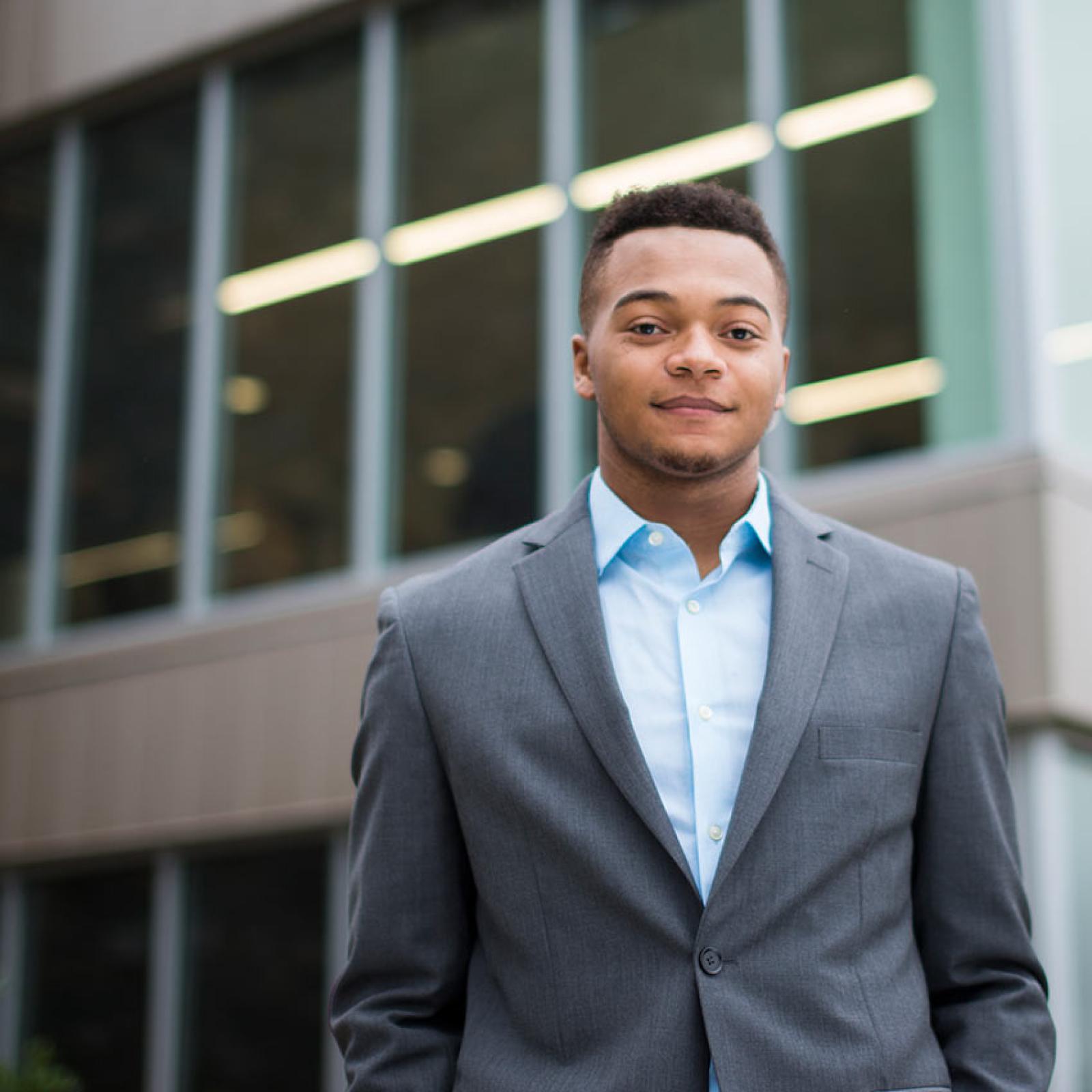 A Pace University student wearing a suit stands in front of a building