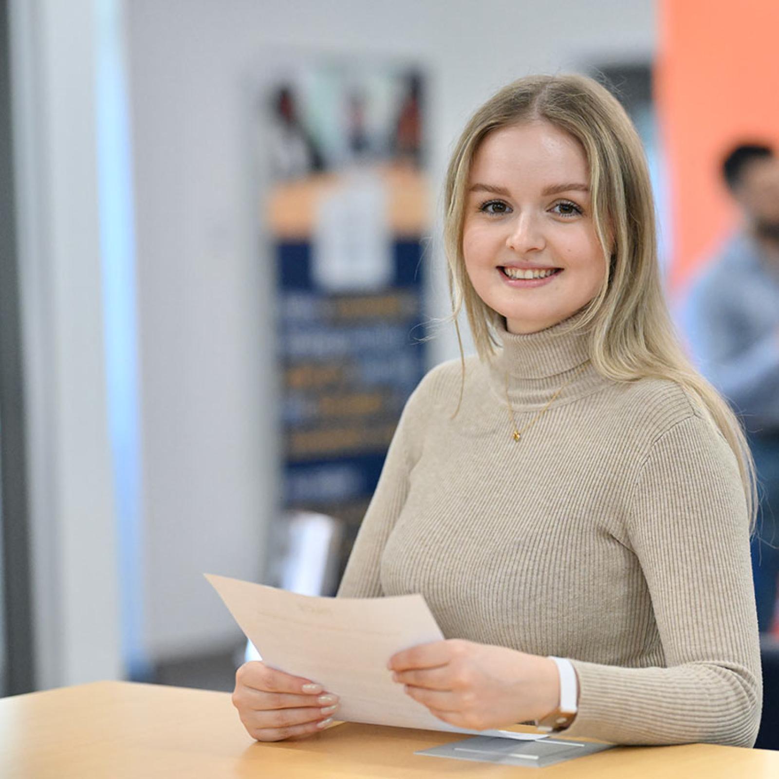 A Pace University student holds a paper and smiles