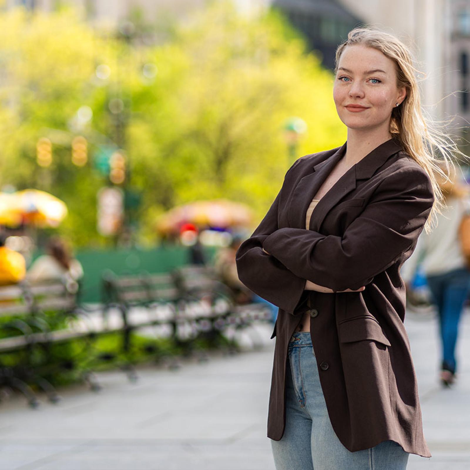 A Pace student stands in an outdoor space with her arms crossed