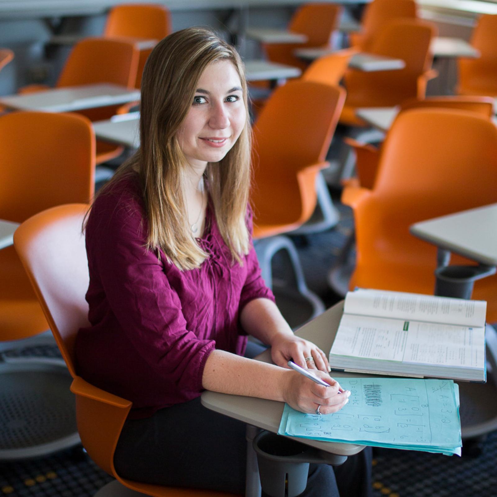 A Pace University teaching student sitting in a classroom surrounded by empty desks.