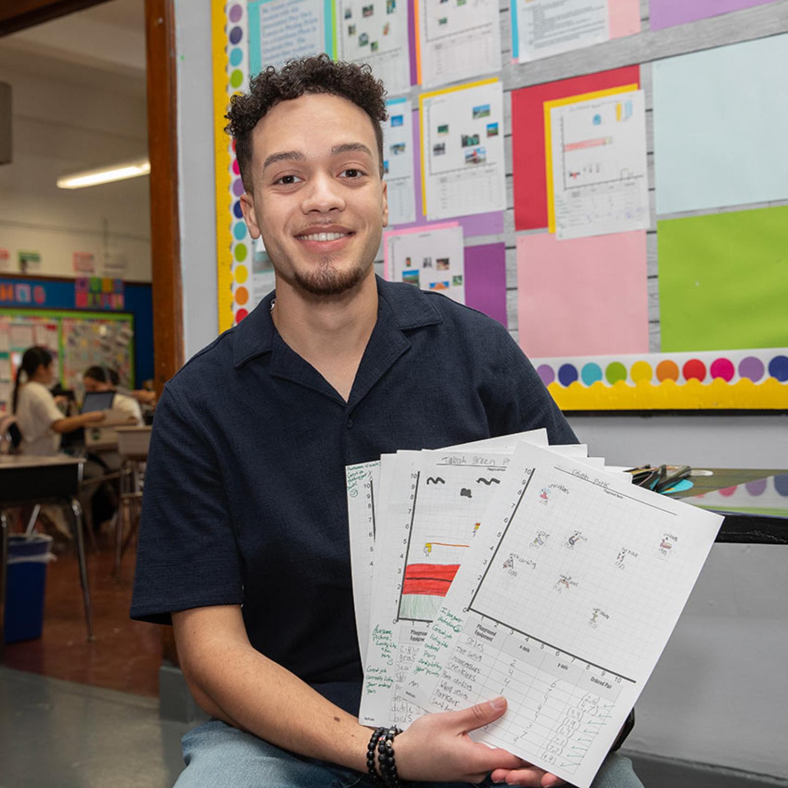 A Pace University student teachers holds up assignments in an elementary school hallway.