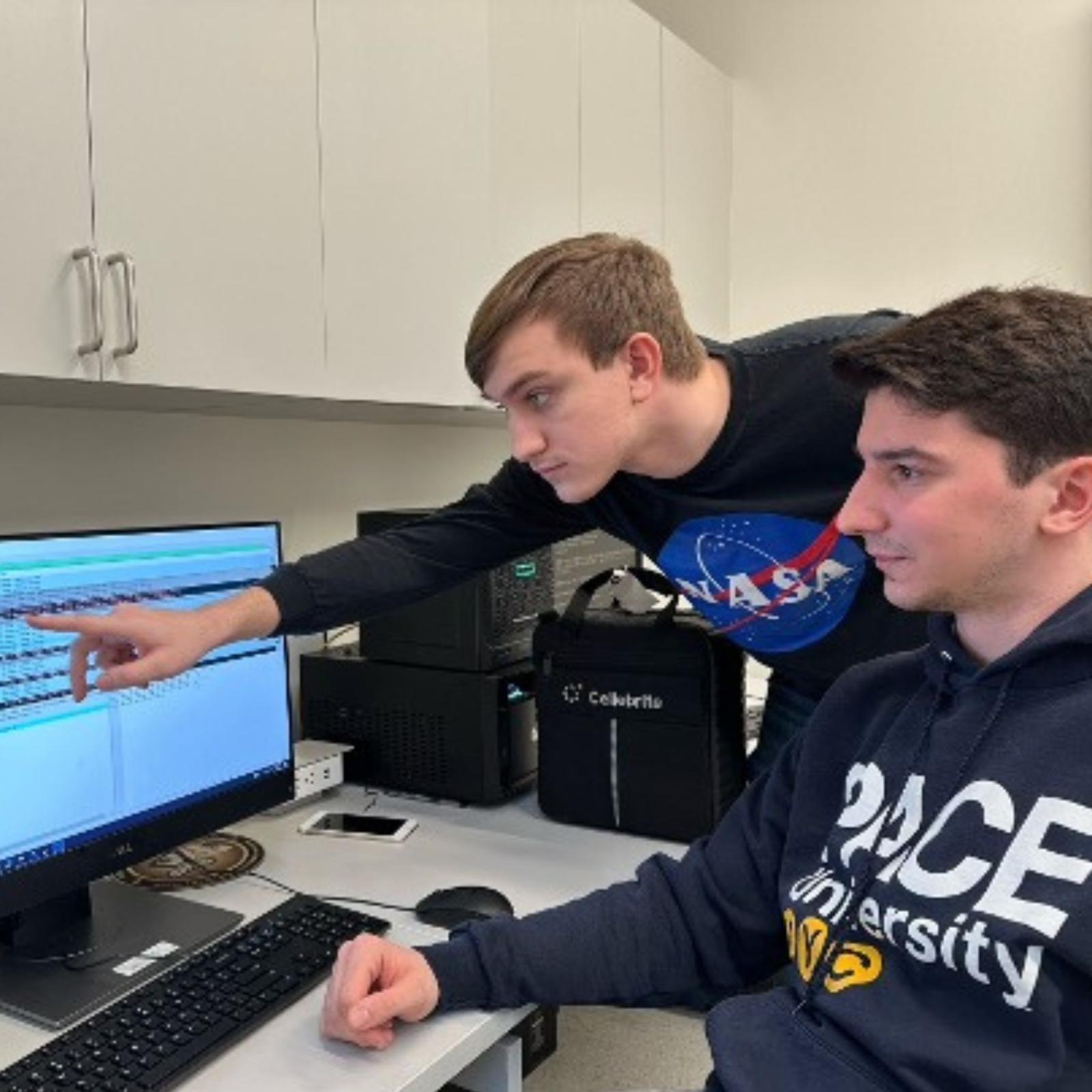Two Seidenberg students working in the Digital Forensics Research lab and chatting while looking at a computer screen.