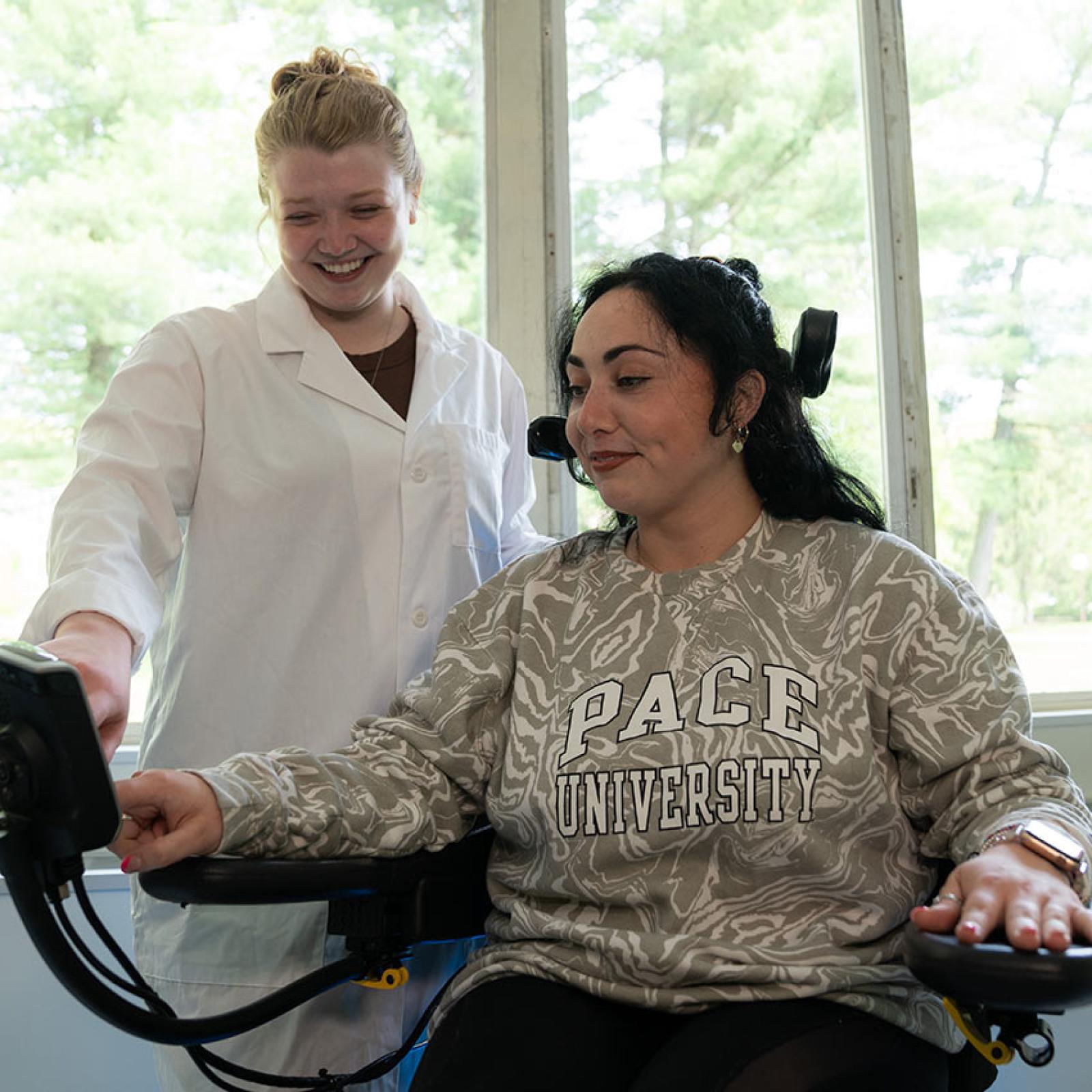 Pace University student helping a person navigate a tablet on her wheelchair.