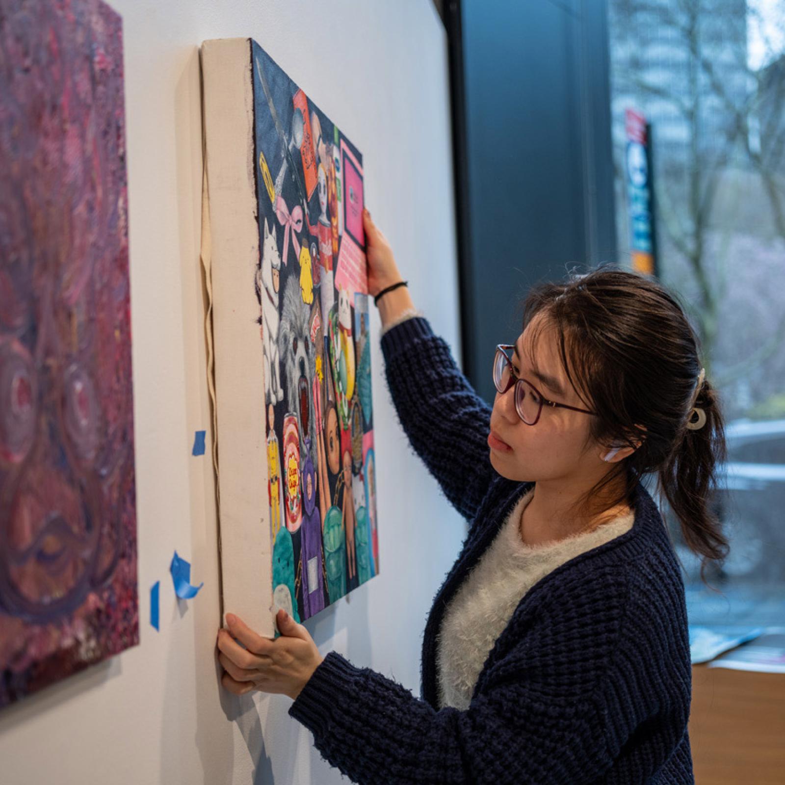 A Pace University art student hanging a canvas on a wall.