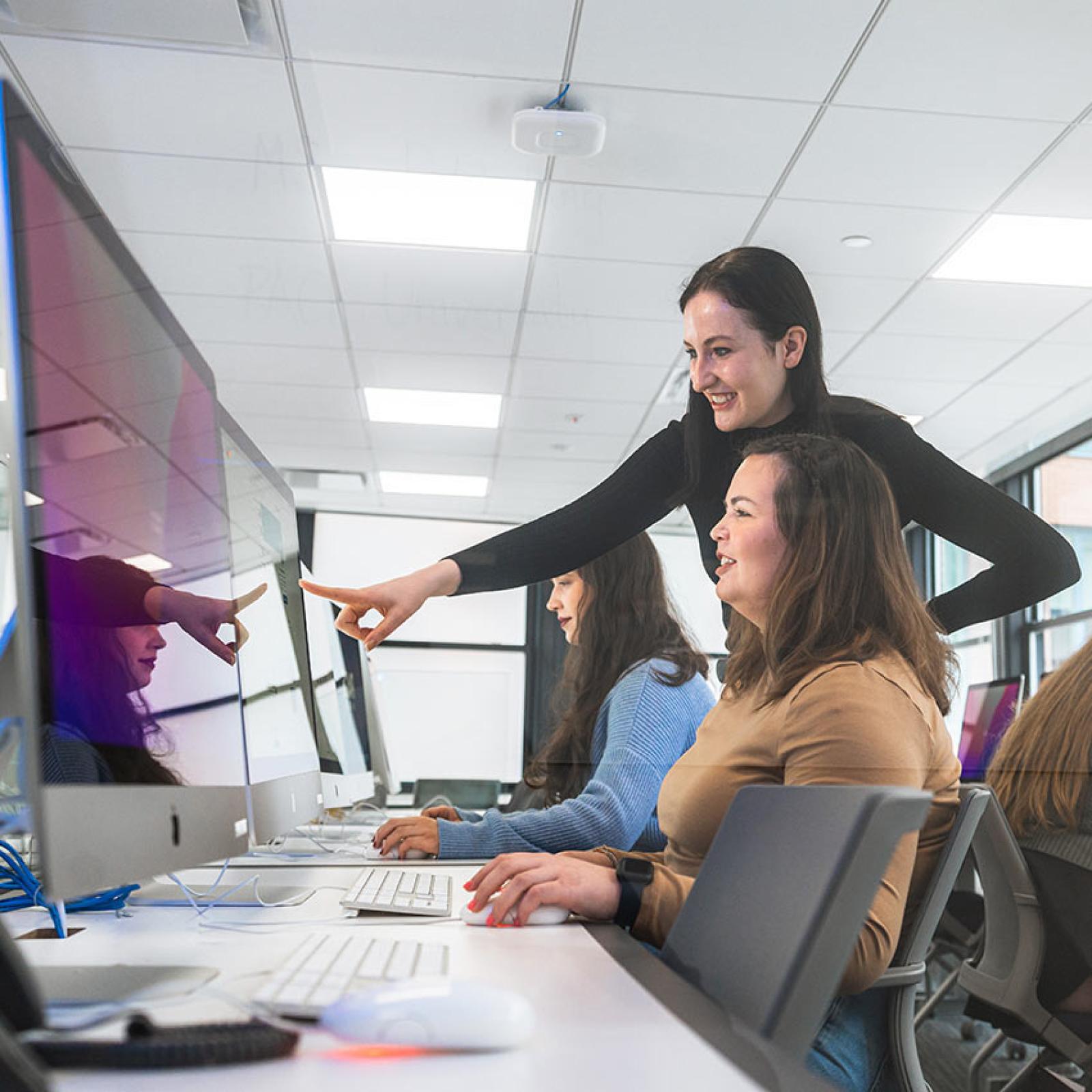 A Pace University faculty member points to a computer screen while talking with a Pace student.