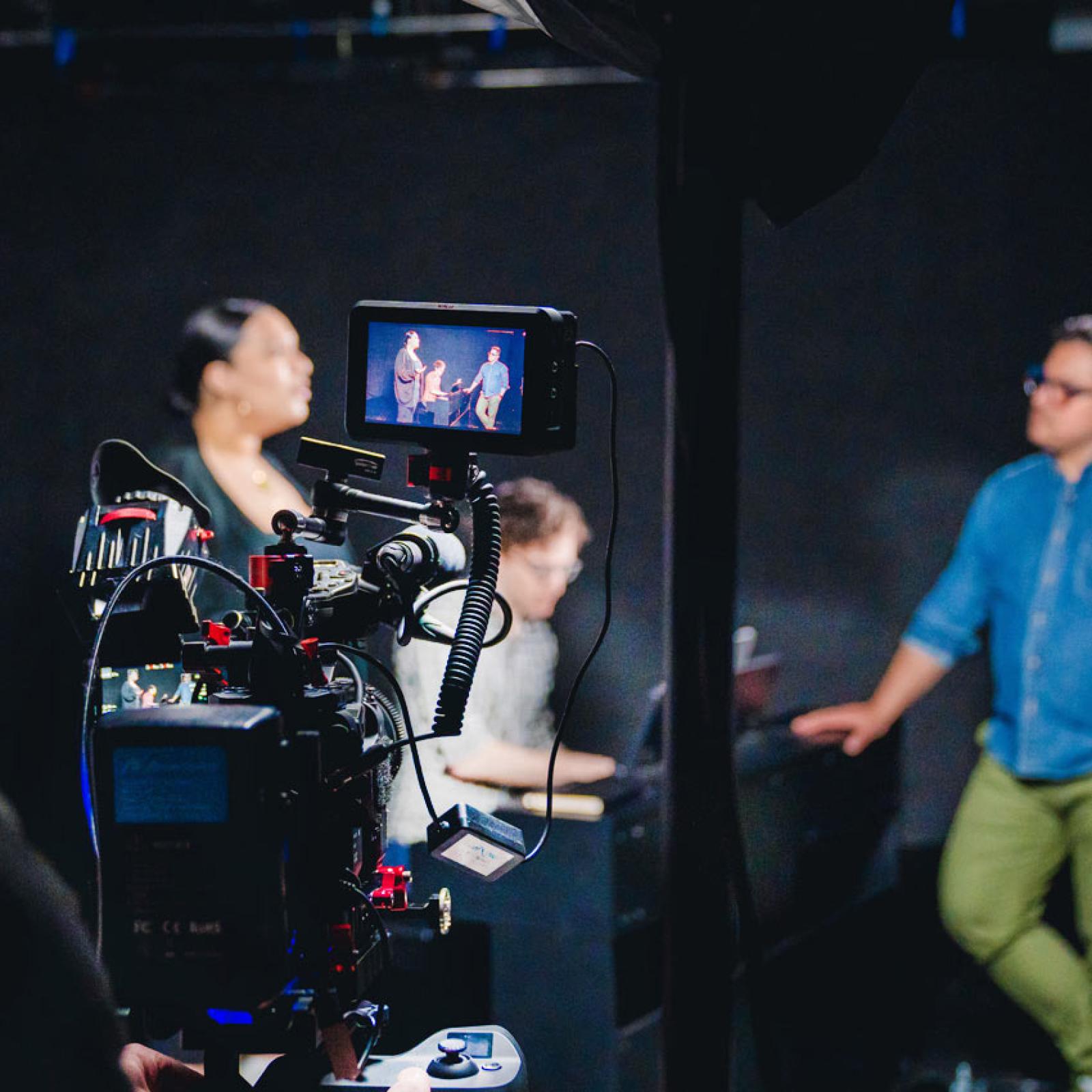 A professional video camera with people in the preview screen.