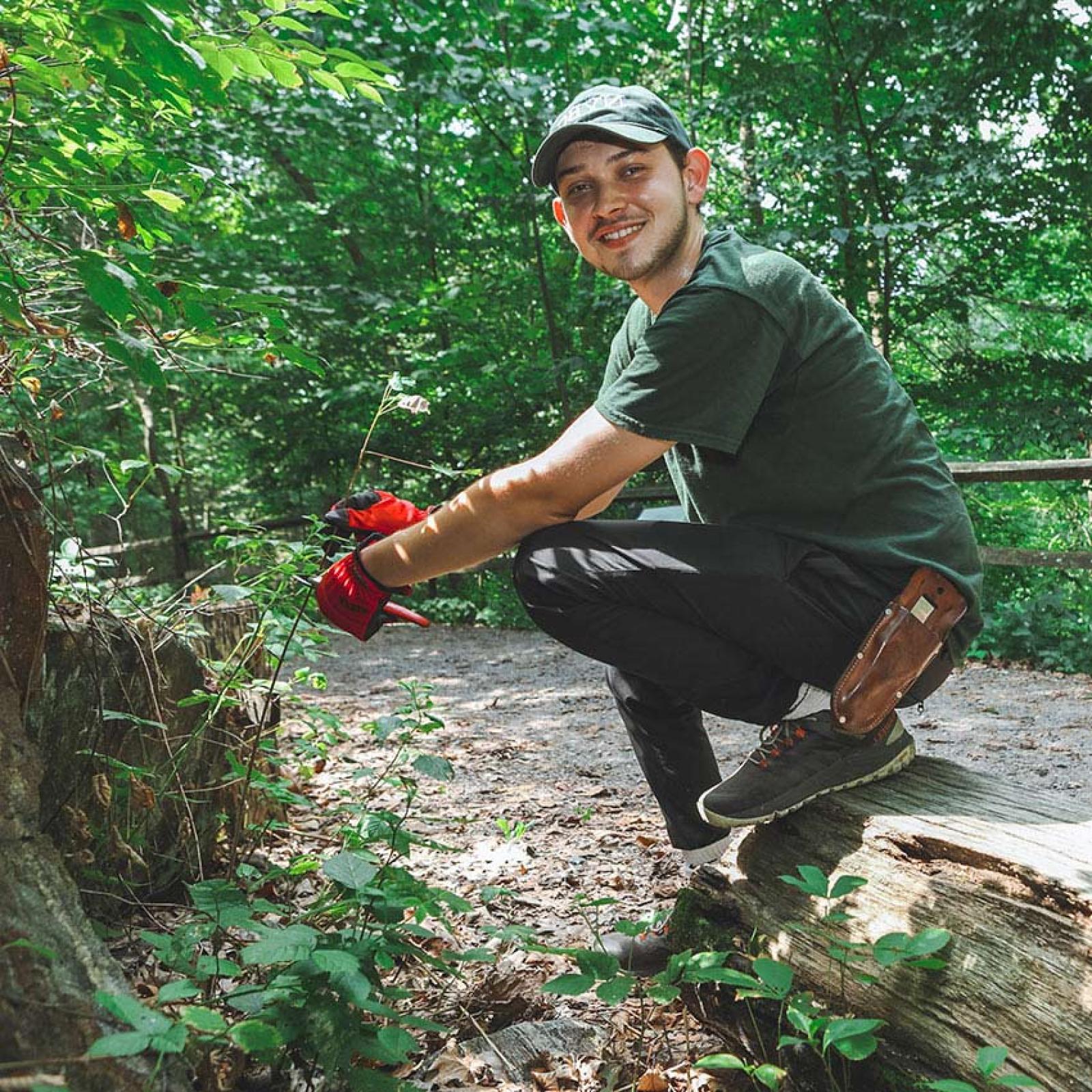 A Pace University student kneels outdoors with work gloves.