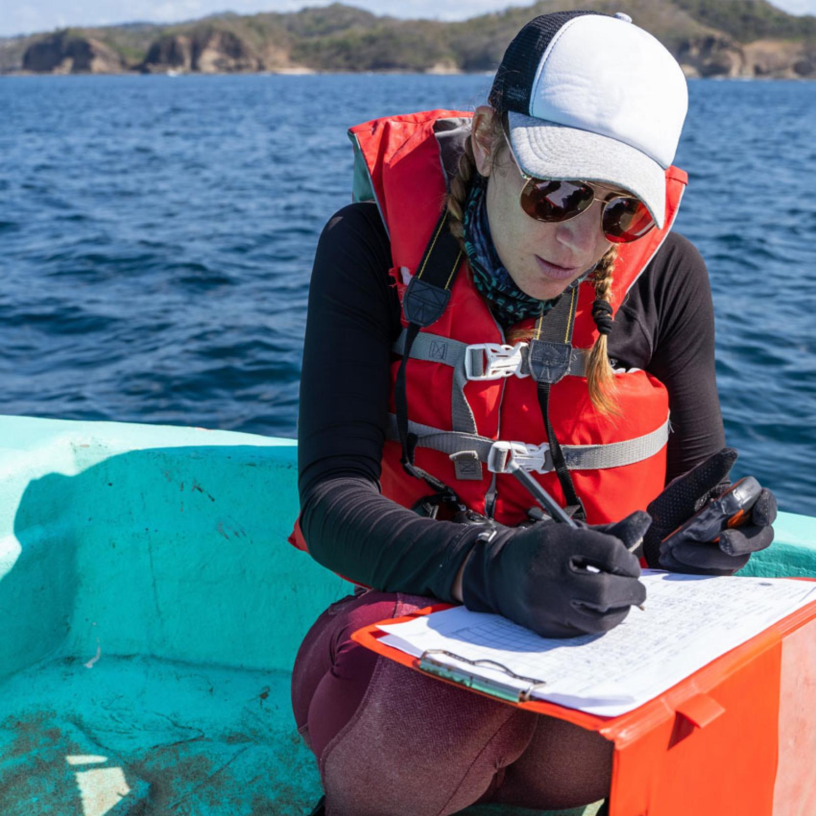 Woman on a boat recording data on a clipboard.