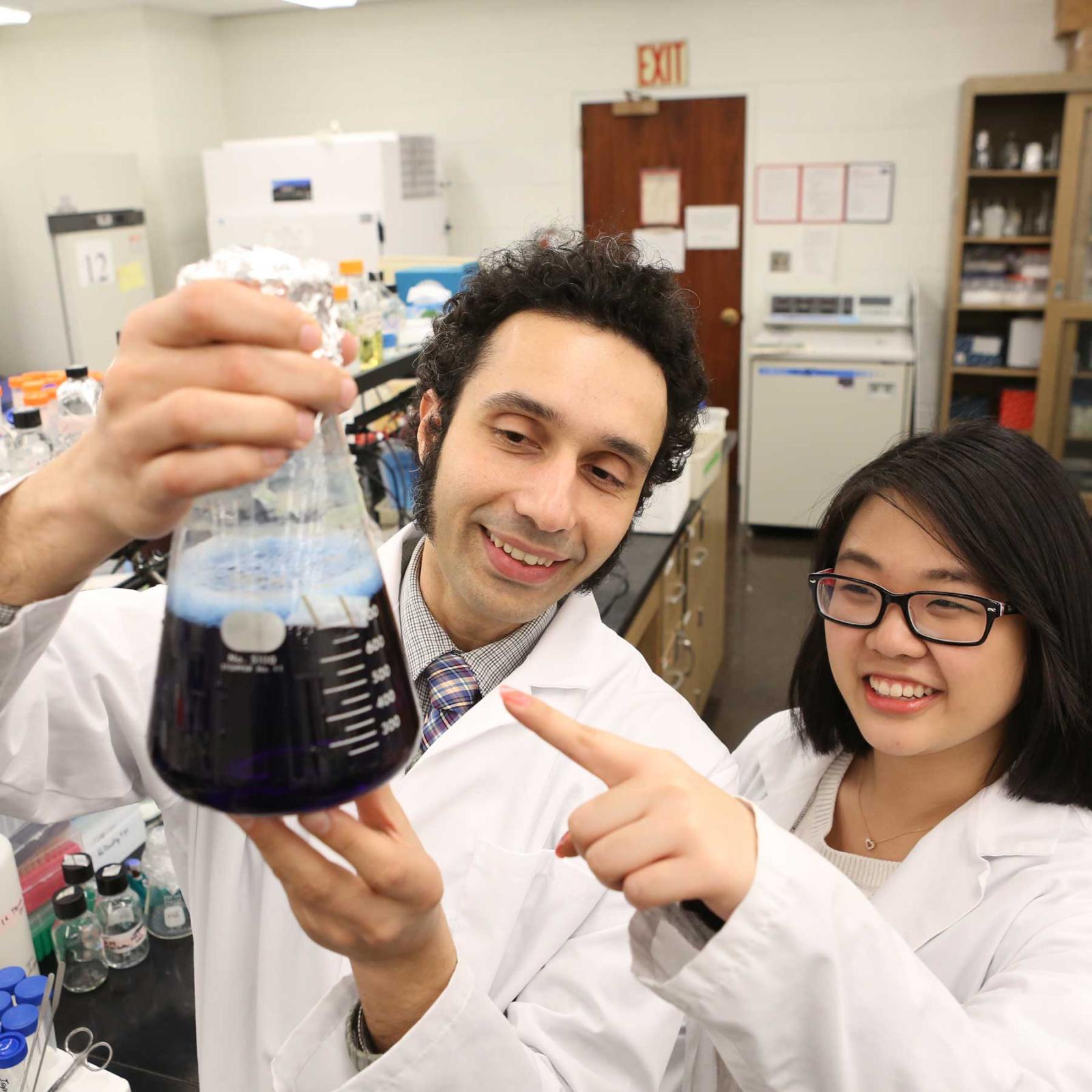 Pace University Biology professor Zafir Buraei with student looking at a flask with liquid inside