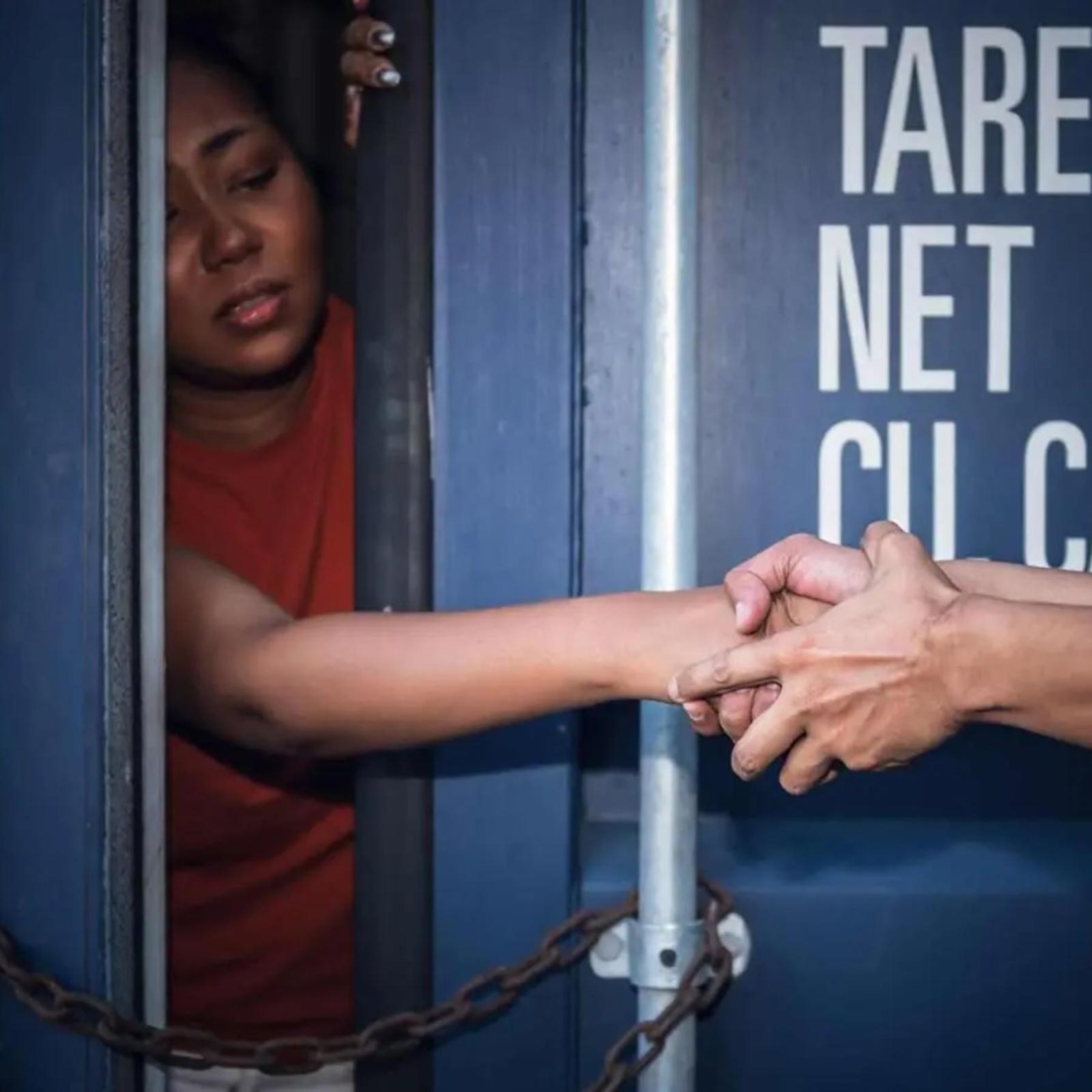A woman inside a shipping container reaching out to grasping hands.