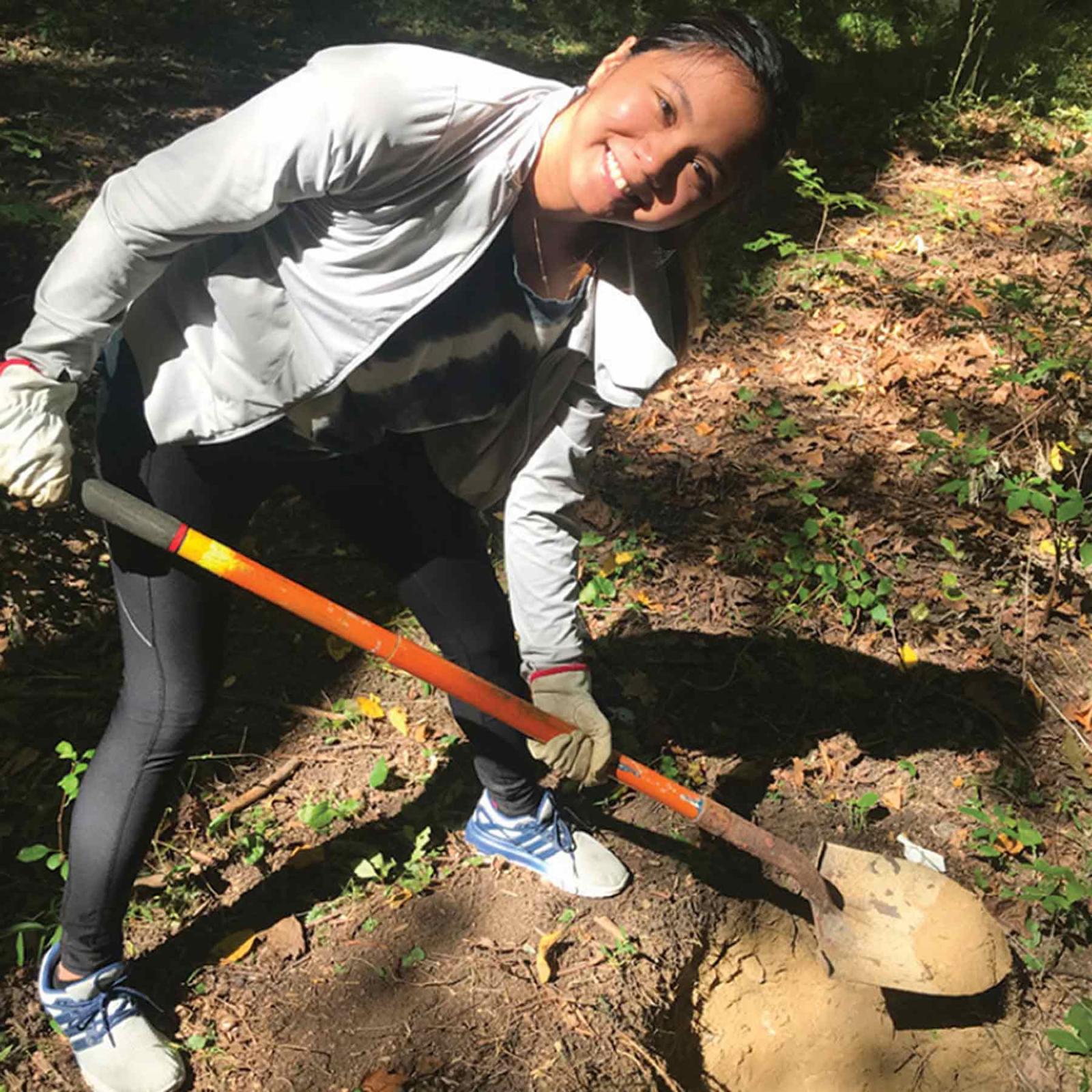 Pace University female student smiling, shoveling dirt
