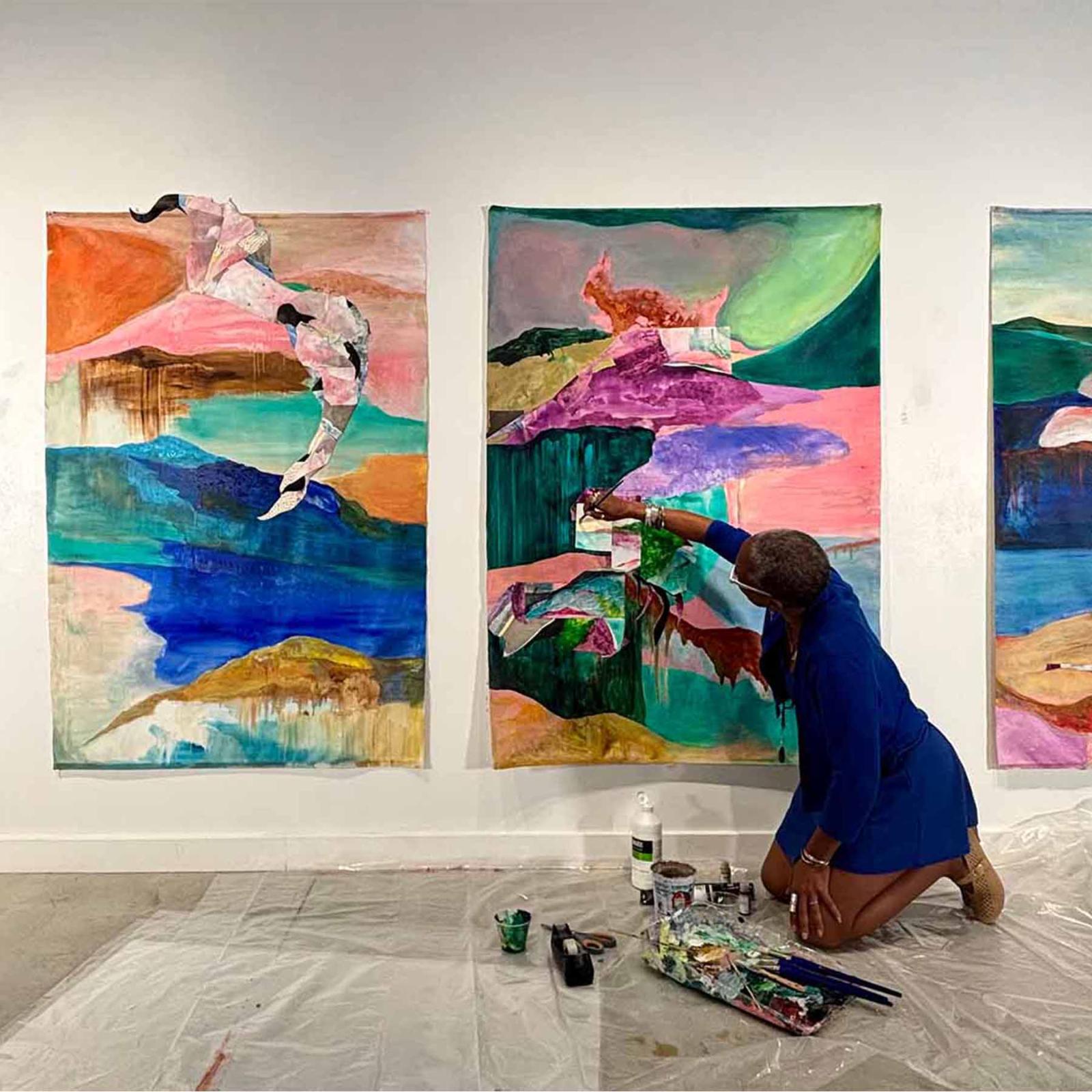 La Vaughn Belle kneels in front of a series of her paintings.