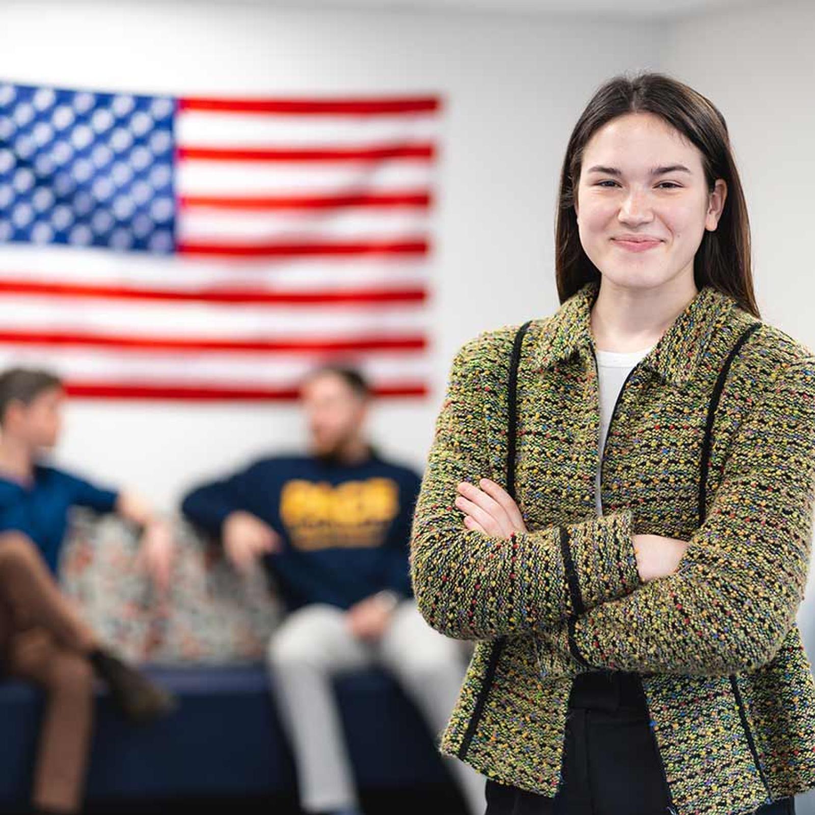 Pace University student standing in front of the USA flag, smiling at the camera.