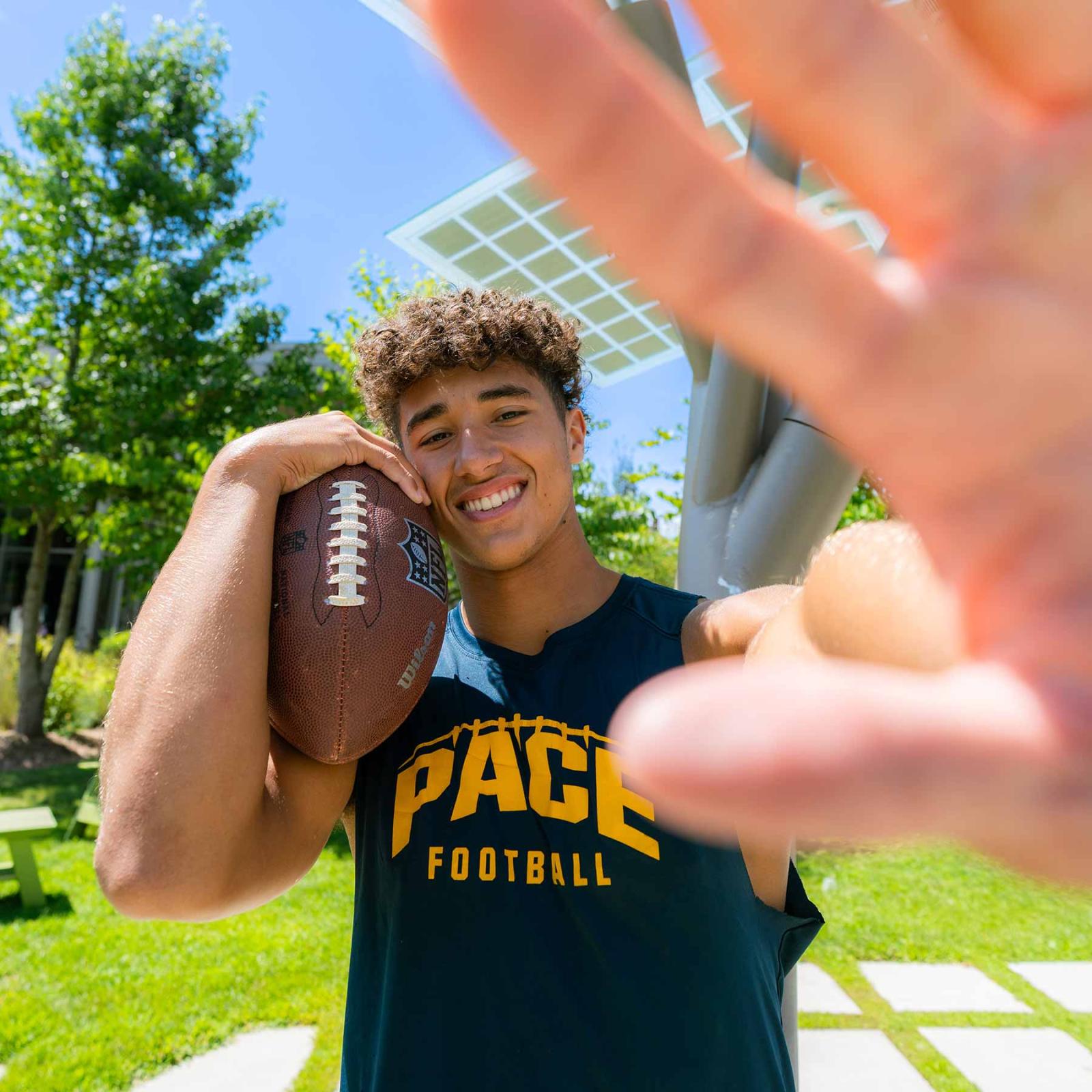 Pace University football player holding a football, smiling at the camera.