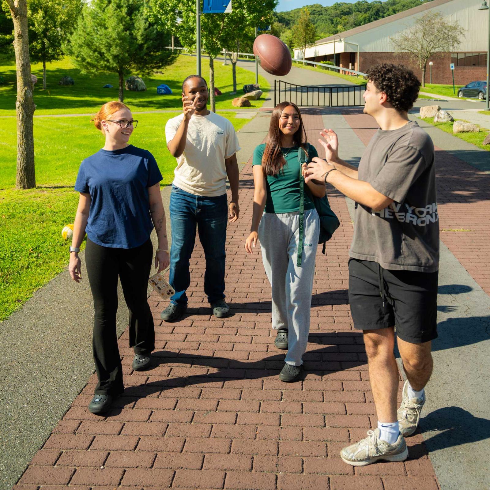 Group of Pace University students walking around the Westchester campus tossing a football.