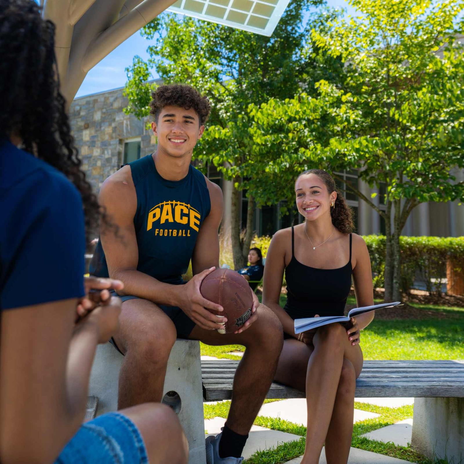 Two Pace University students at the Westchester campus, one is holding a football and the other one is holding a book.