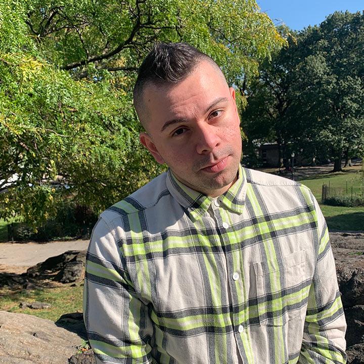 Alumnus Marcos Gonsalez in a park wearing a long sleeve dress shirt