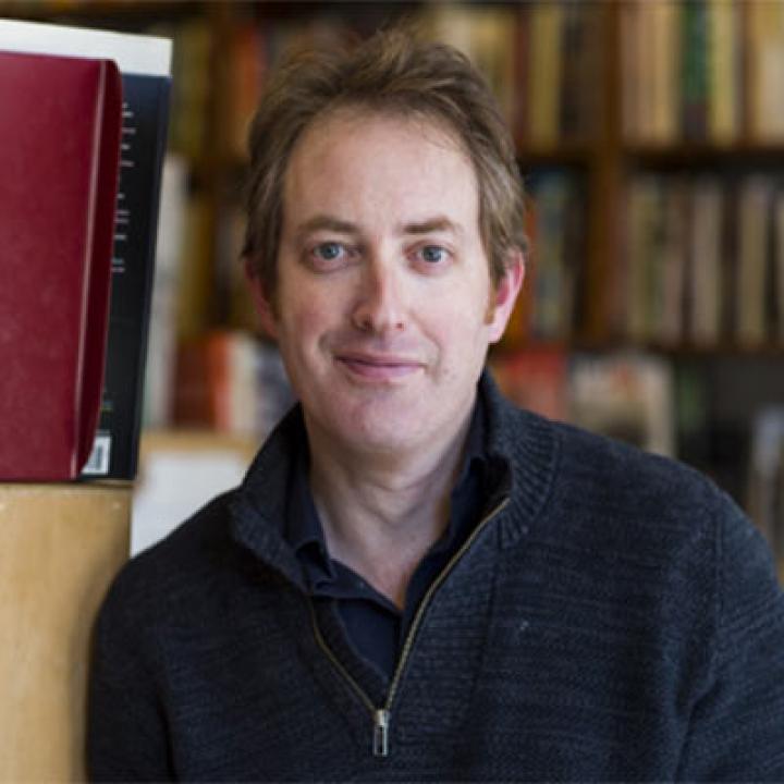 Portrait of Miles Knable wearing a black zippered pullover with books in the background
